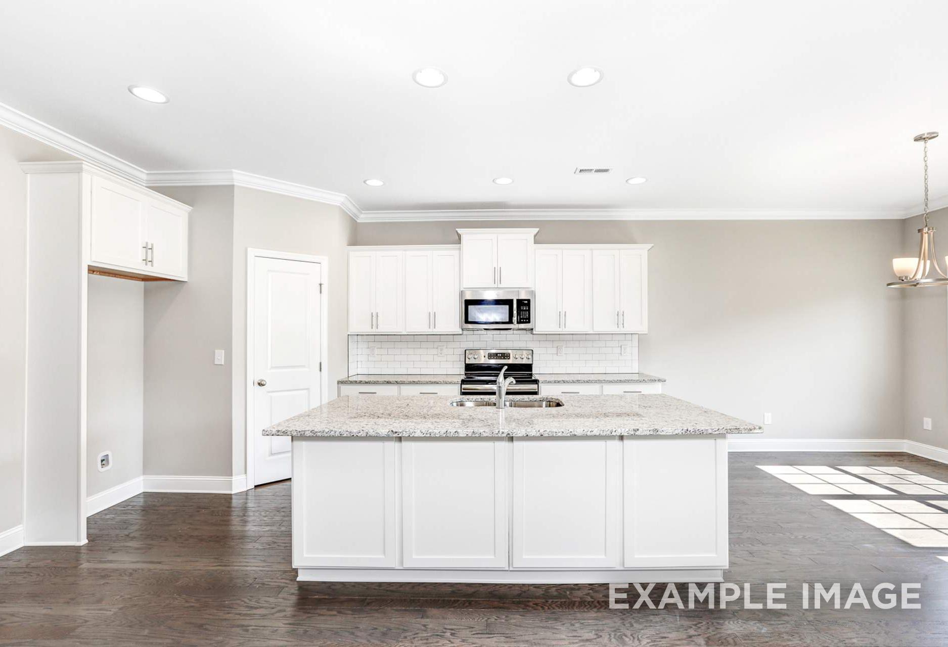 Spacious white kitchen in The Montgomery B by Davidson Homes, featuring granite island, stainless appliances, and hardwood floors