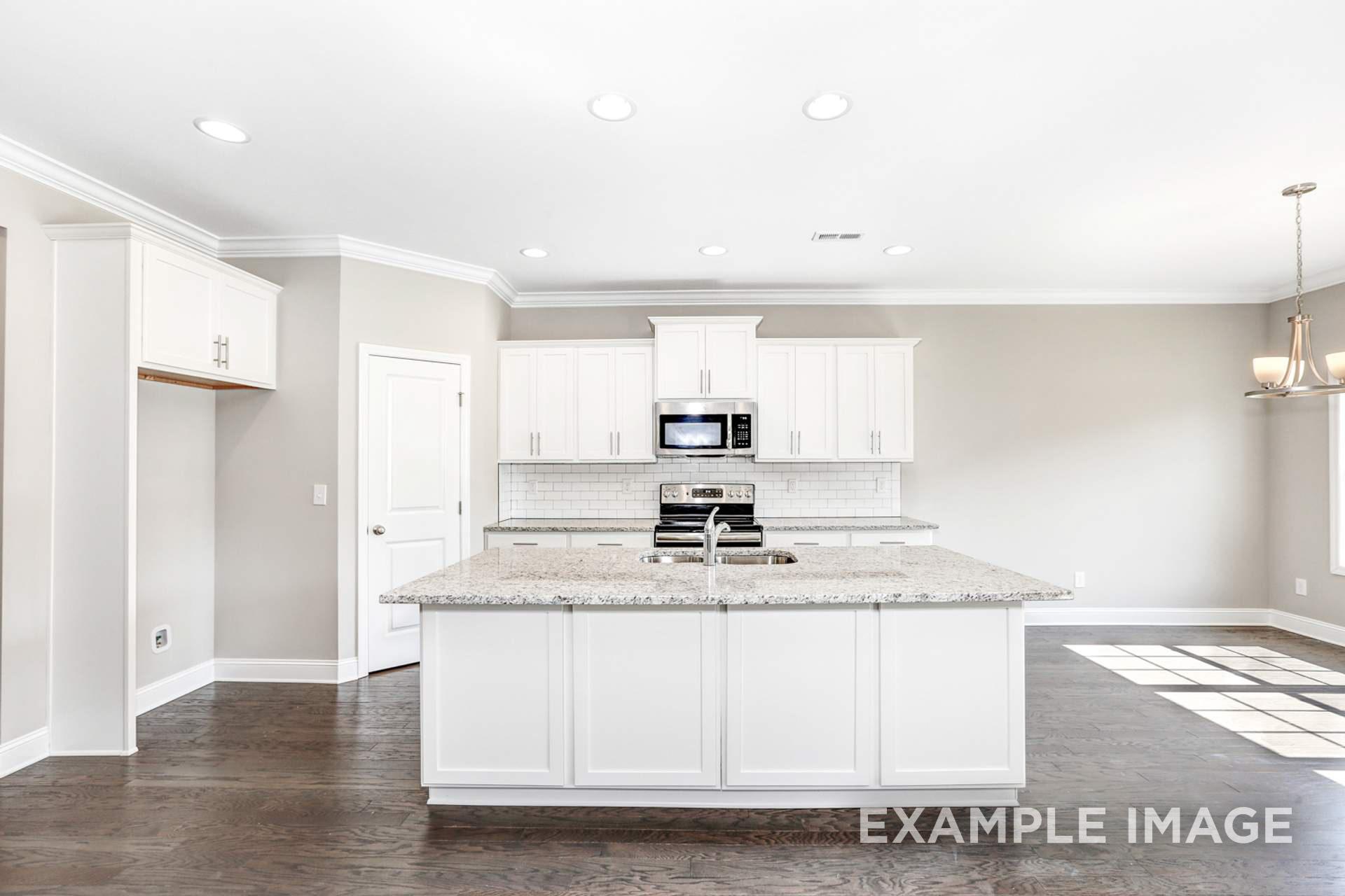 Spacious white kitchen in The Montgomery B by Davidson Homes, featuring granite island, stainless appliances, and hardwood floors