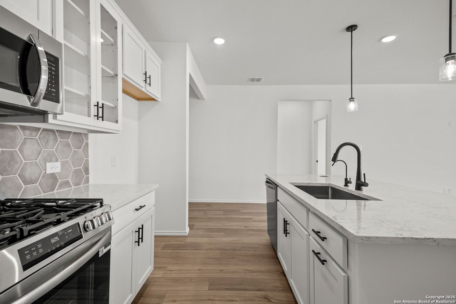 Modern white kitchen with quartz island, stainless appliances, hexagon tile backsplash in Davidson Homes The Daphne K, San Antonio