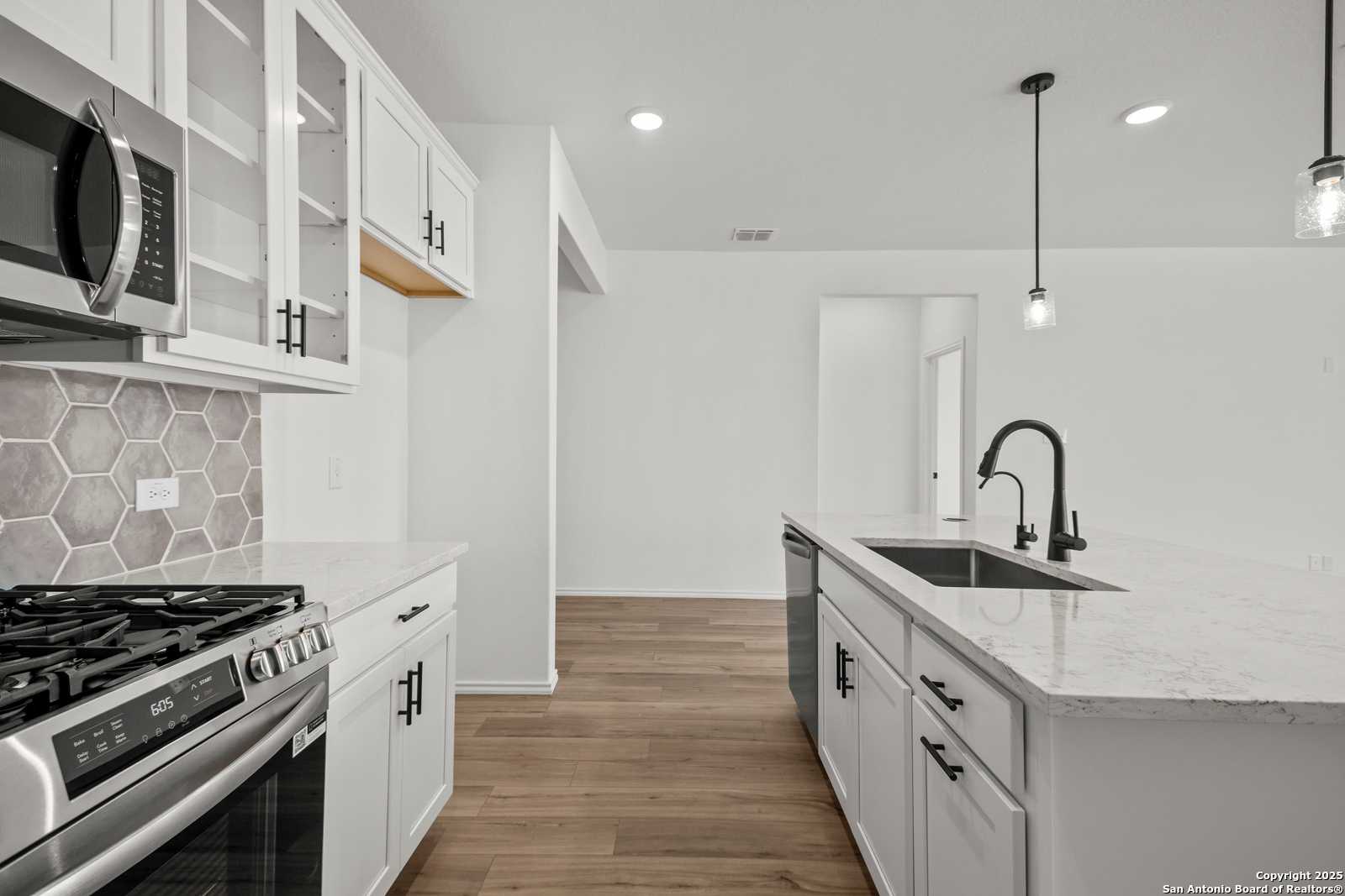 Modern white kitchen with quartz island, stainless appliances, hexagon tile backsplash in Davidson Homes The Daphne K, San Antonio