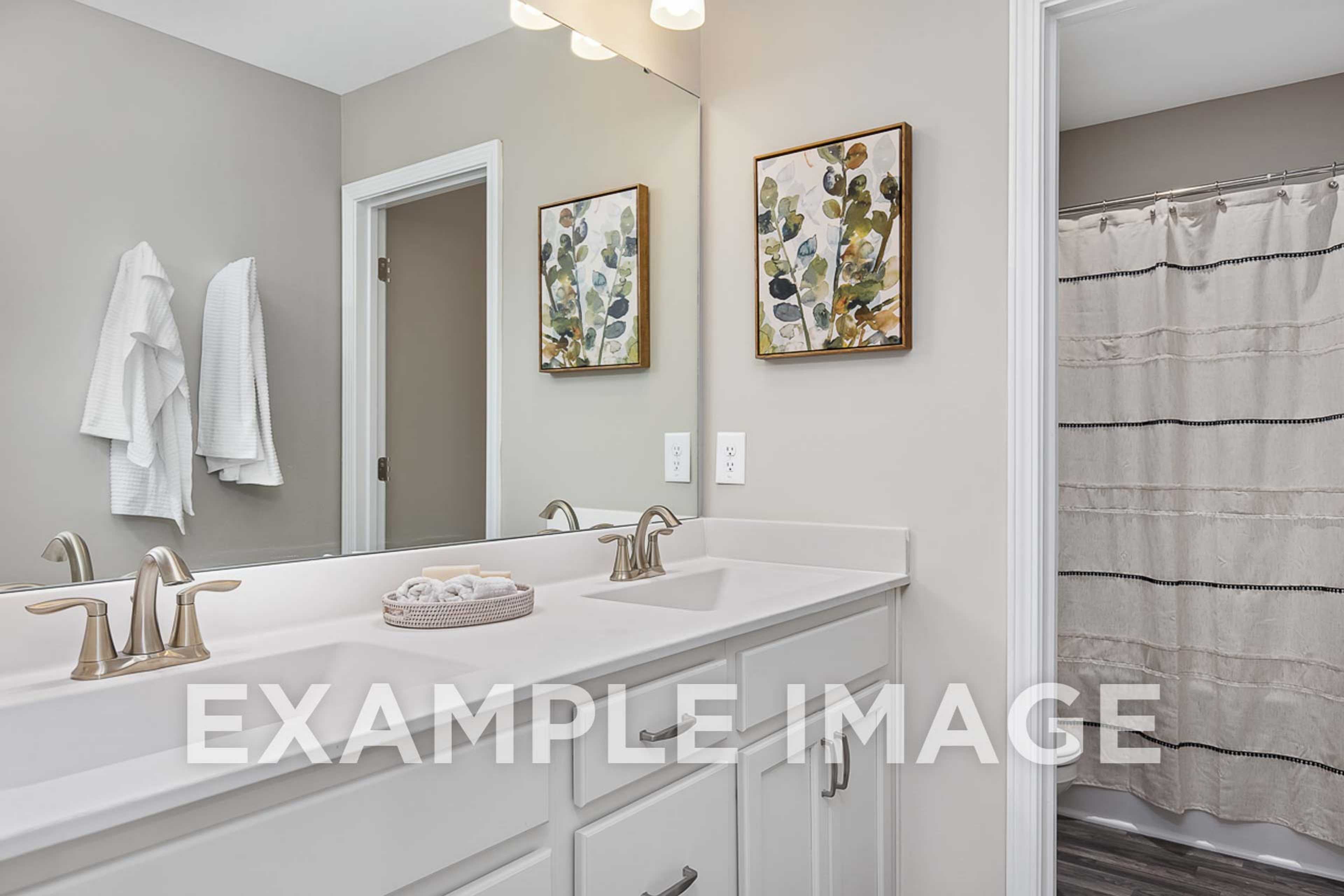 Spacious master bathroom in The Ash home design with double vanity, gray walls, and striped shower curtain