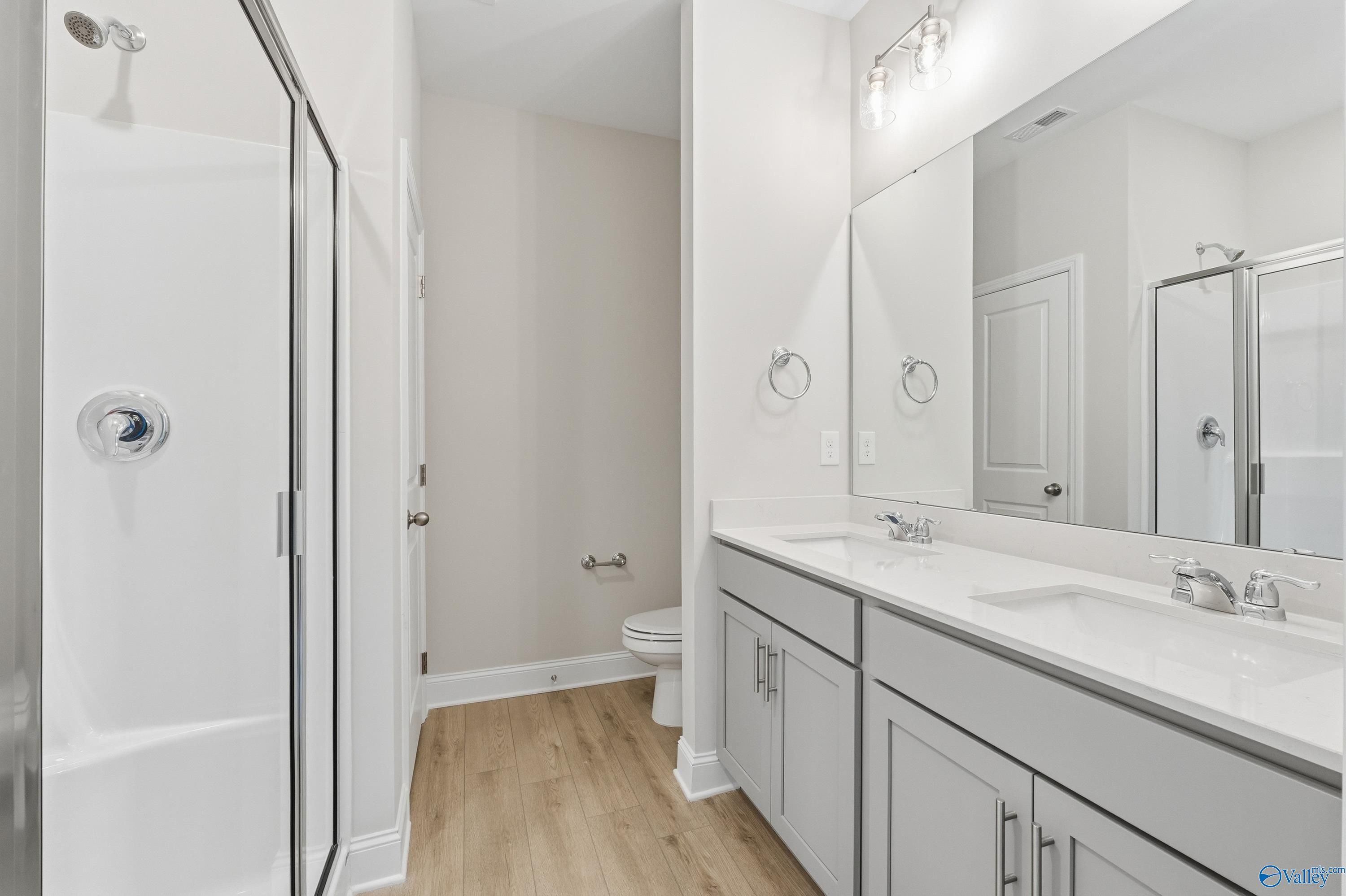 Modern bathroom with double vanity, large mirror, walk-in shower, and gray cabinets in Davidson Homes The Butler, Toney, Alabama