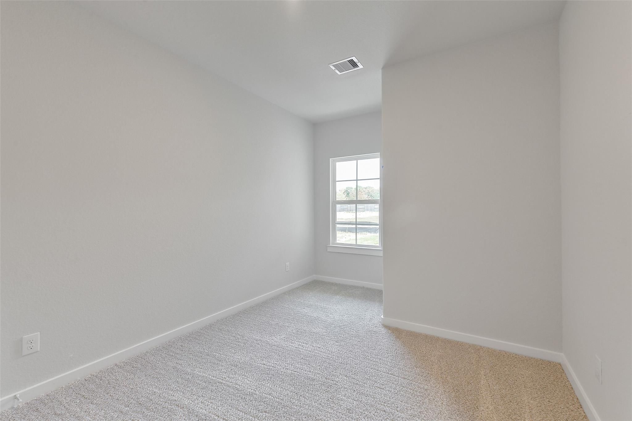 Bright empty secondary bedroom with light gray walls, beige carpet, and large window in Davidson Homes The Colorado G, Magnolia TX