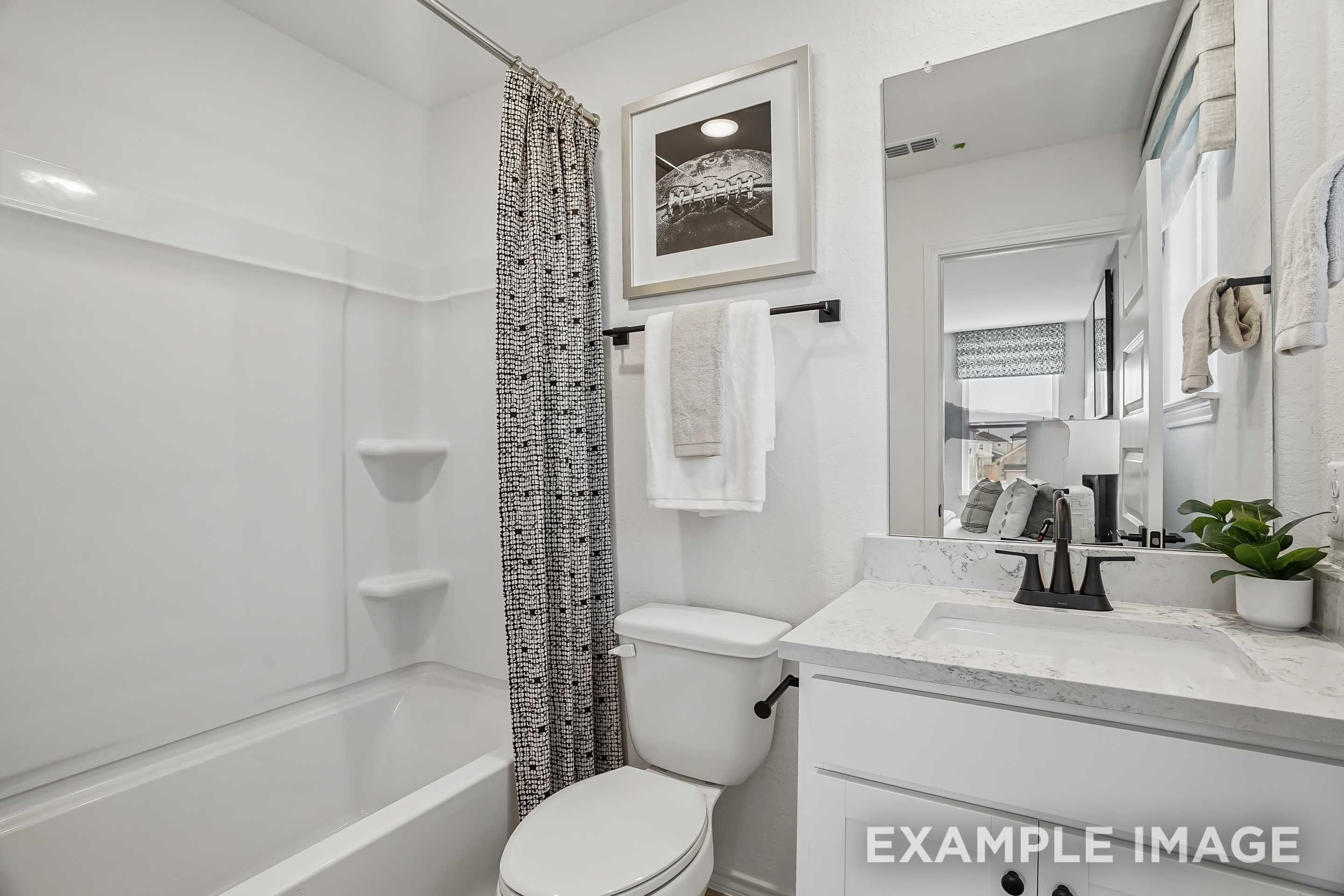 Modern bathroom in The Pinecrest home design featuring a white vanity, marble countertop, and tub-shower combination.
