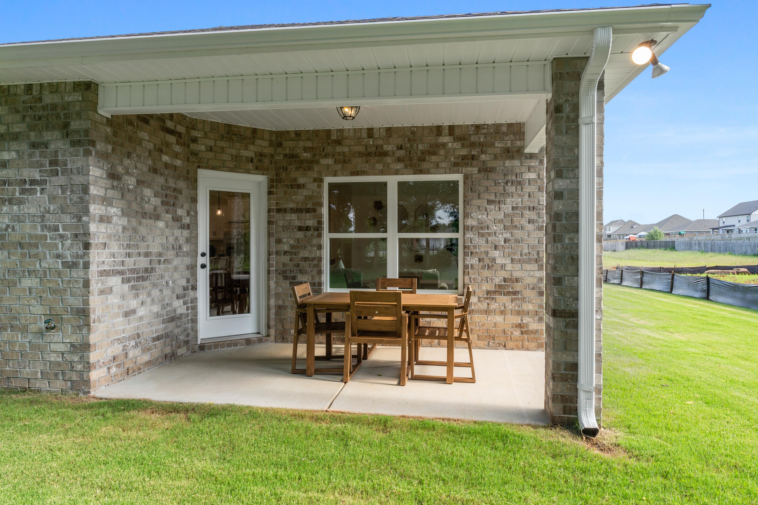 Covered patio with brick exterior, glass door, windows, and wooden dining set overlooking green lawn at Lynn Meadows, Meridianville AL