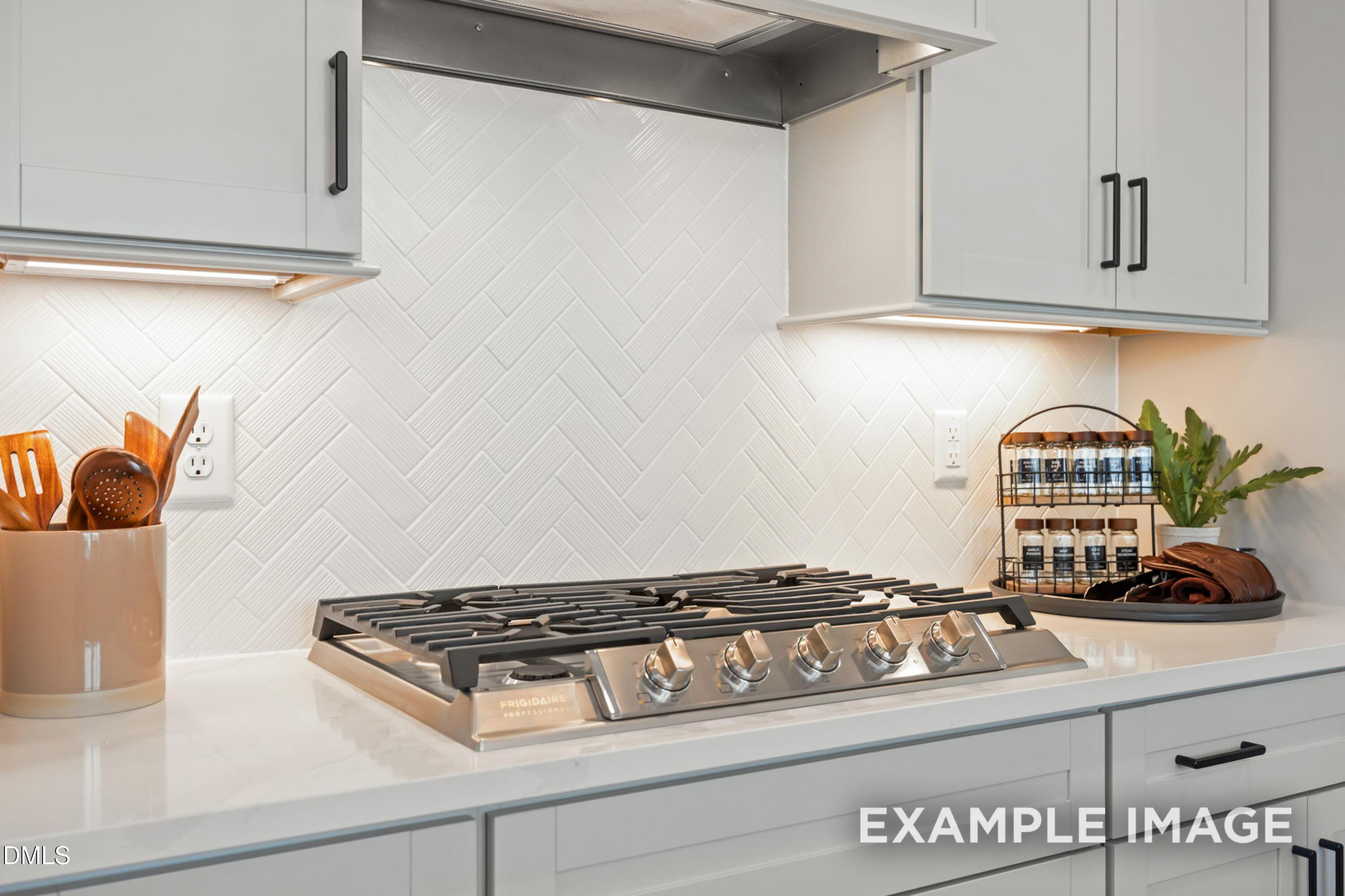 Modern kitchen with herringbone white tile backsplash, Frigidaire gas cooktop, and gray cabinets in Davidson Homes The Mitchell, Knightdale, NC