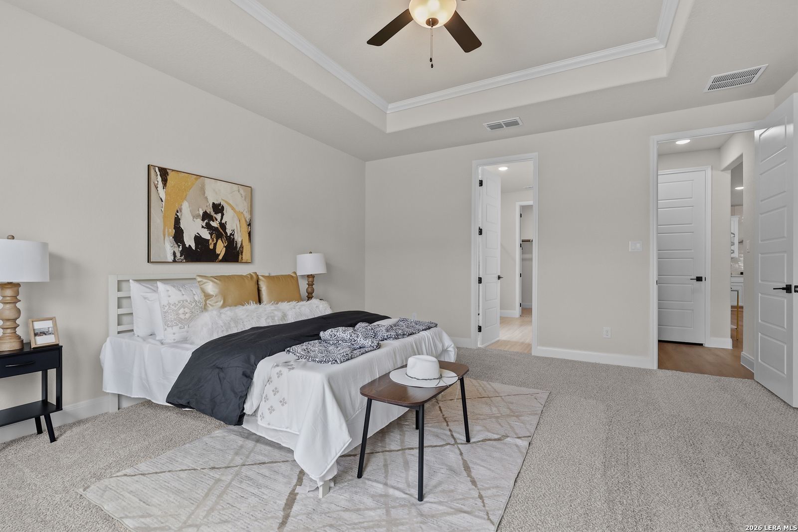 Elegant master bedroom with king bed, gold pillows, abstract art, and en-suite doors in Davidson Homes The Lanier G, Castroville, TX