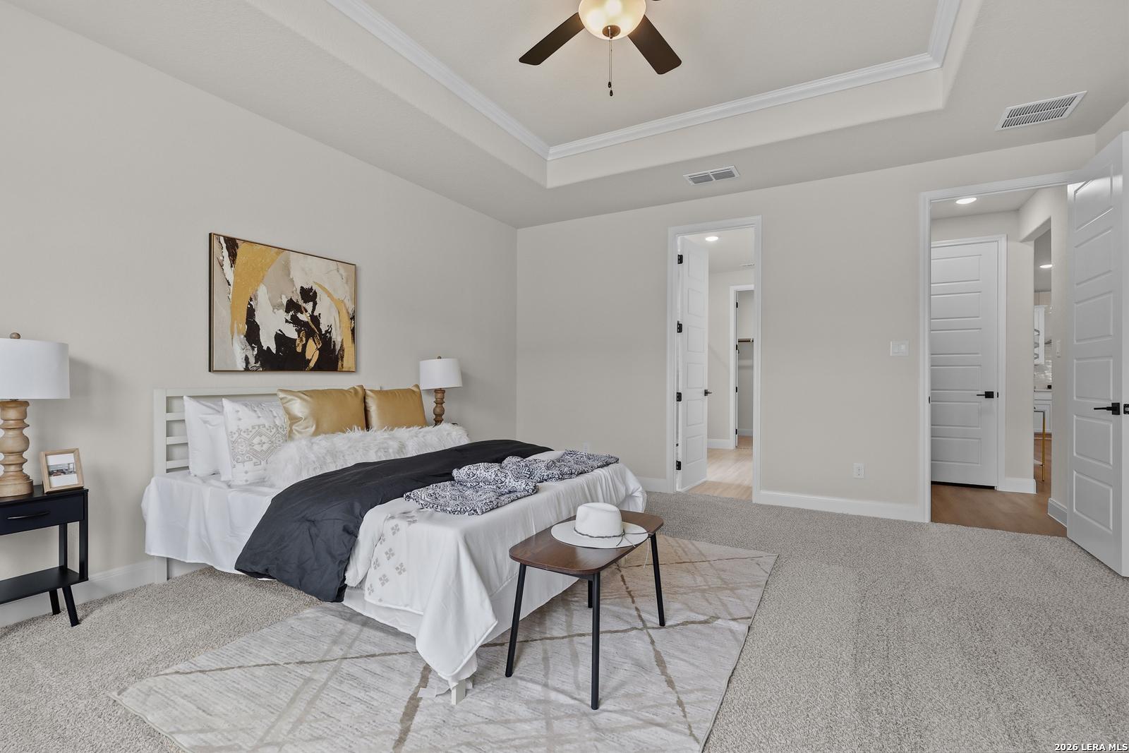 Elegant master bedroom with king bed, gold pillows, abstract art, and en-suite doors in Davidson Homes The Lanier G, Castroville, TX