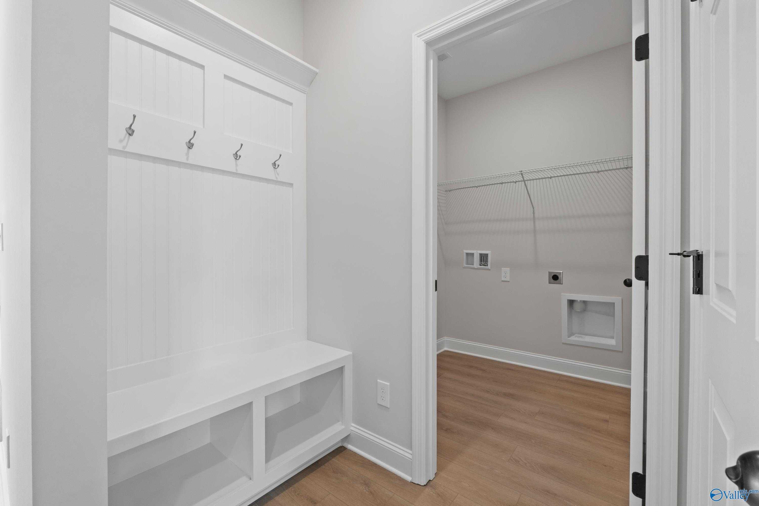 Built-in white mudroom with coat hooks, bench seating, and adjacent laundry area in Davidson Homes The Franklin C, Hazel Green, Alabama