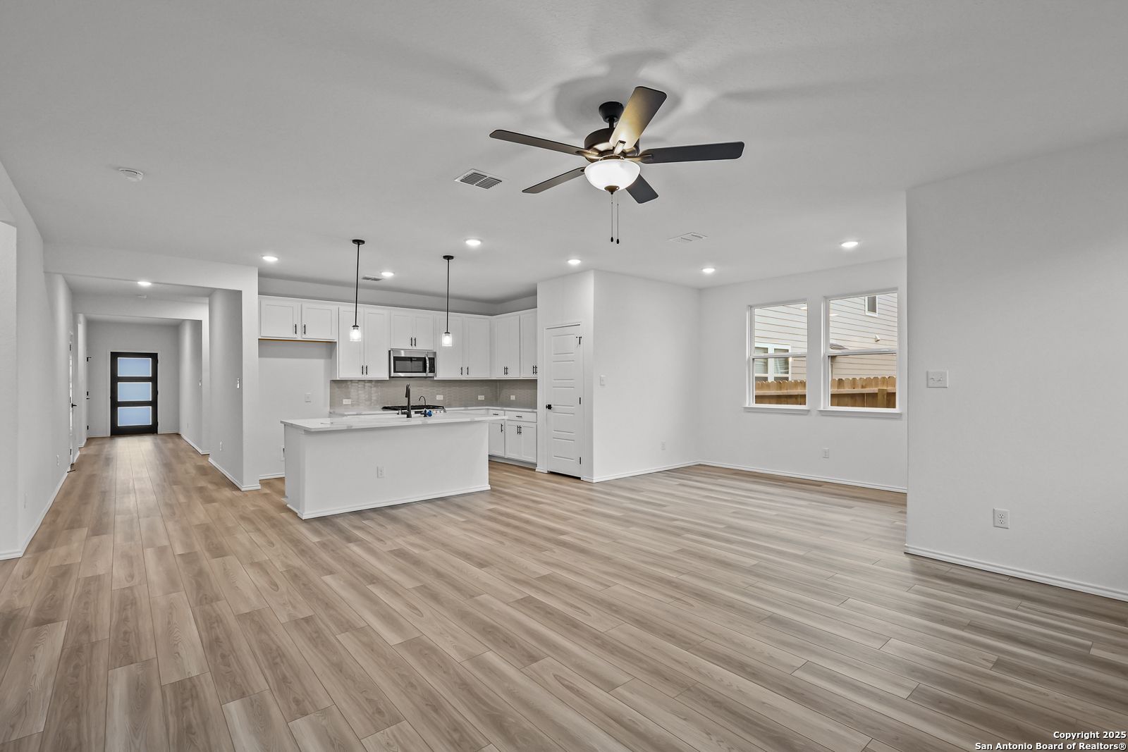 Bright open-concept kitchen and living area with white cabinets, island, and luxury vinyl plank flooring in The Daphne J by Davidson Homes