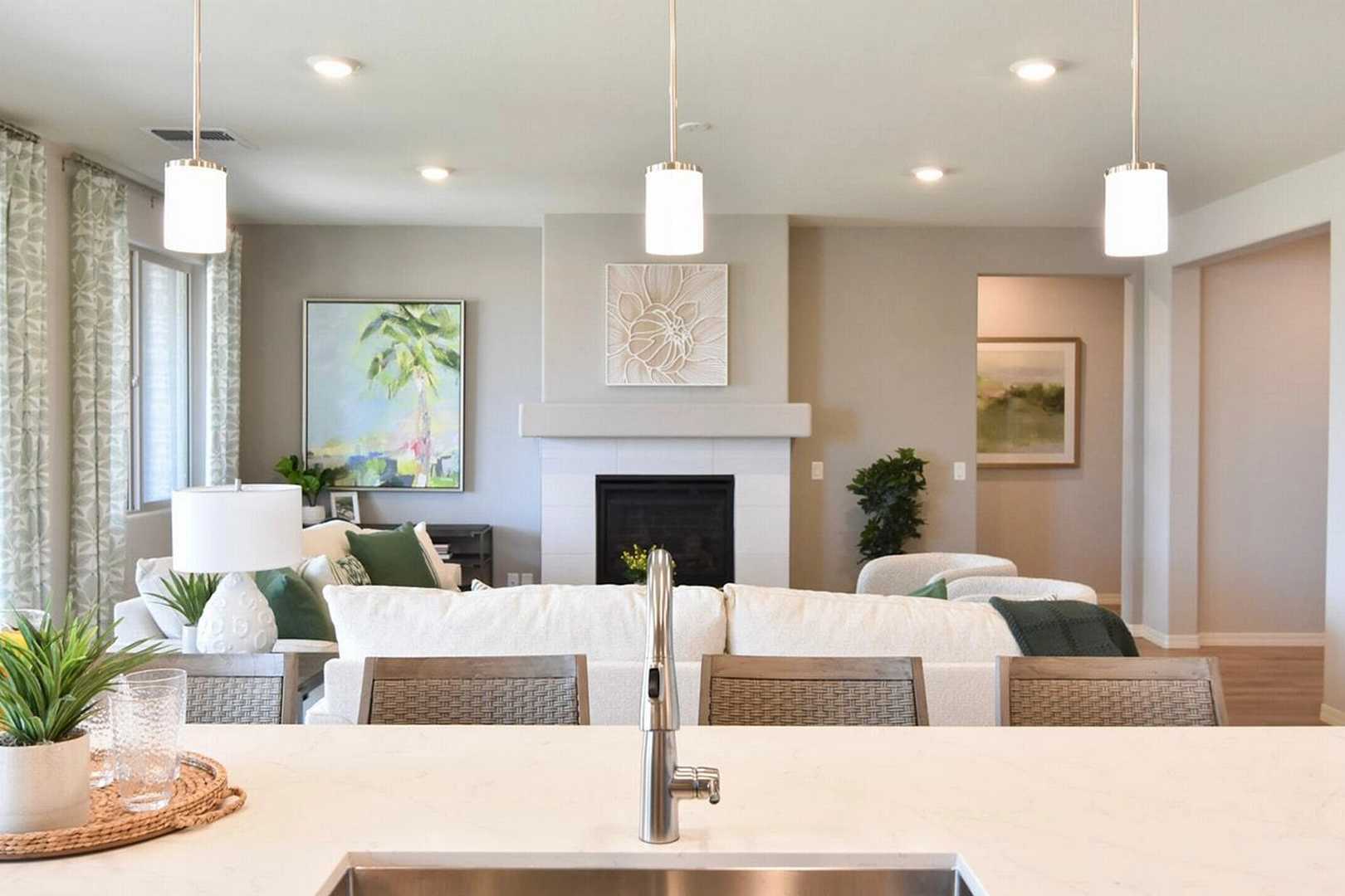 Open-concept kitchen living room at North Ridge Pronghorn Ranch in Prescott Valley AZ with white quartz island, neutral fireplace, and sheer-curtained windows
