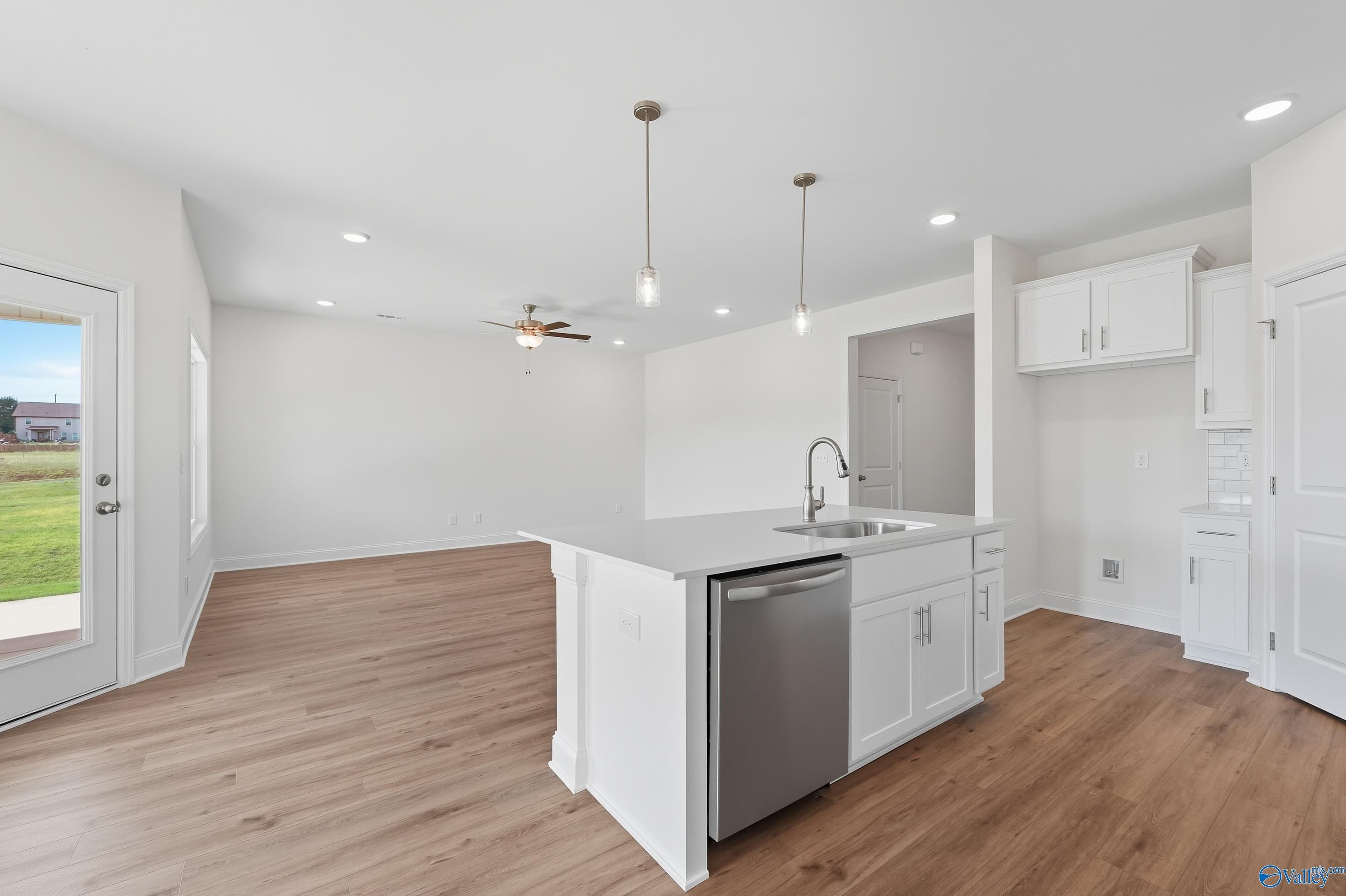 Modern open-concept kitchen with white island sink, stainless dishwasher, pendant lights, and grassy backyard view in The Everett by Davidson Homes, Meridianville, Alabama