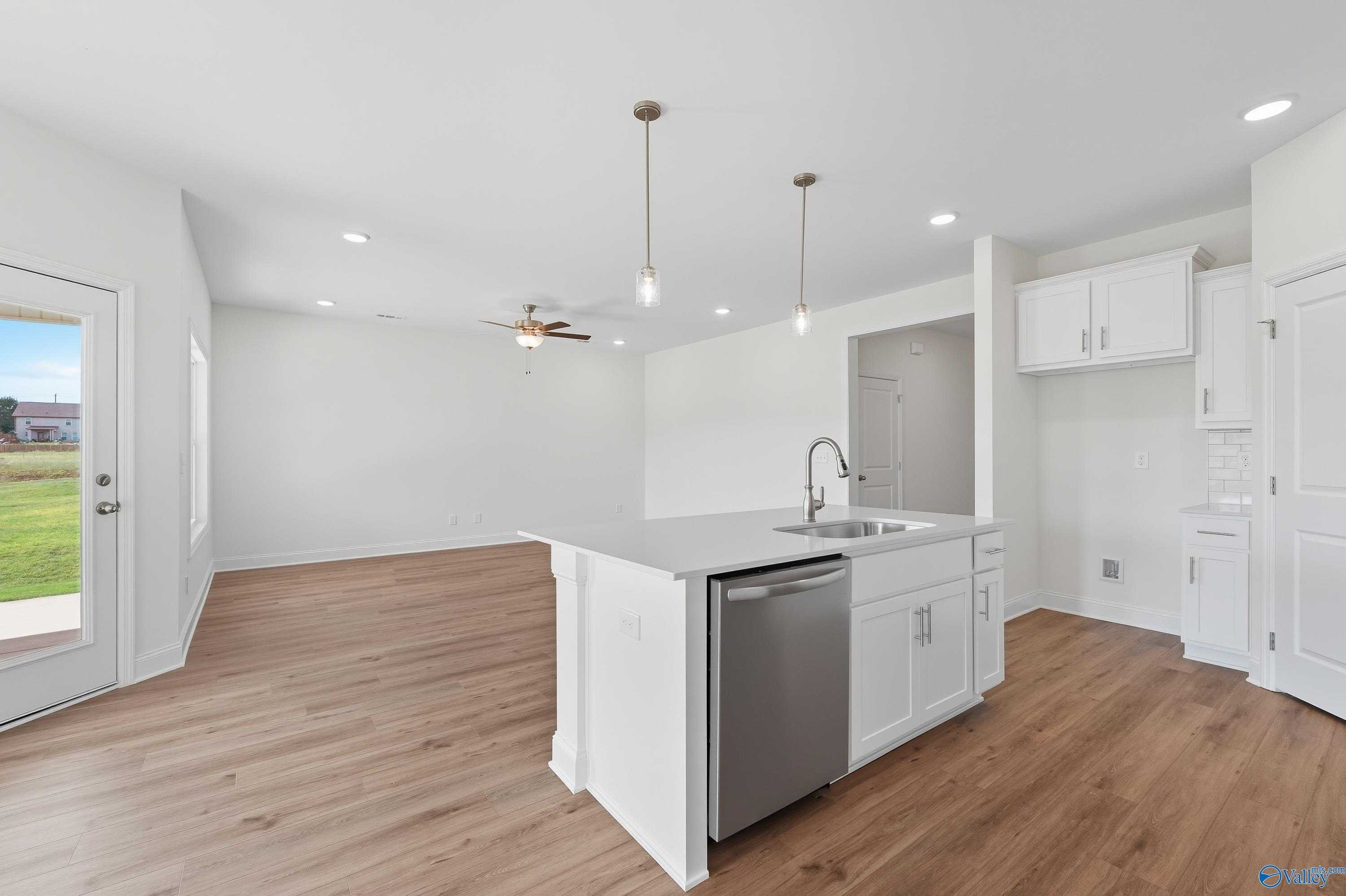 Modern white kitchen with island, stainless dishwasher, pendant lights, and French doors to grassy yard in The Everett by Davidson Homes, Meridianville, AL