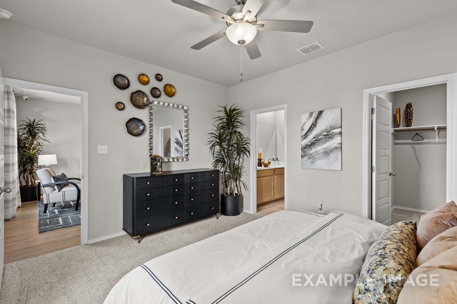 Elegant master bedroom with white king bed, black dresser, potted palms, en-suite bath in Davidson Homes Sabine J, Heartland TX