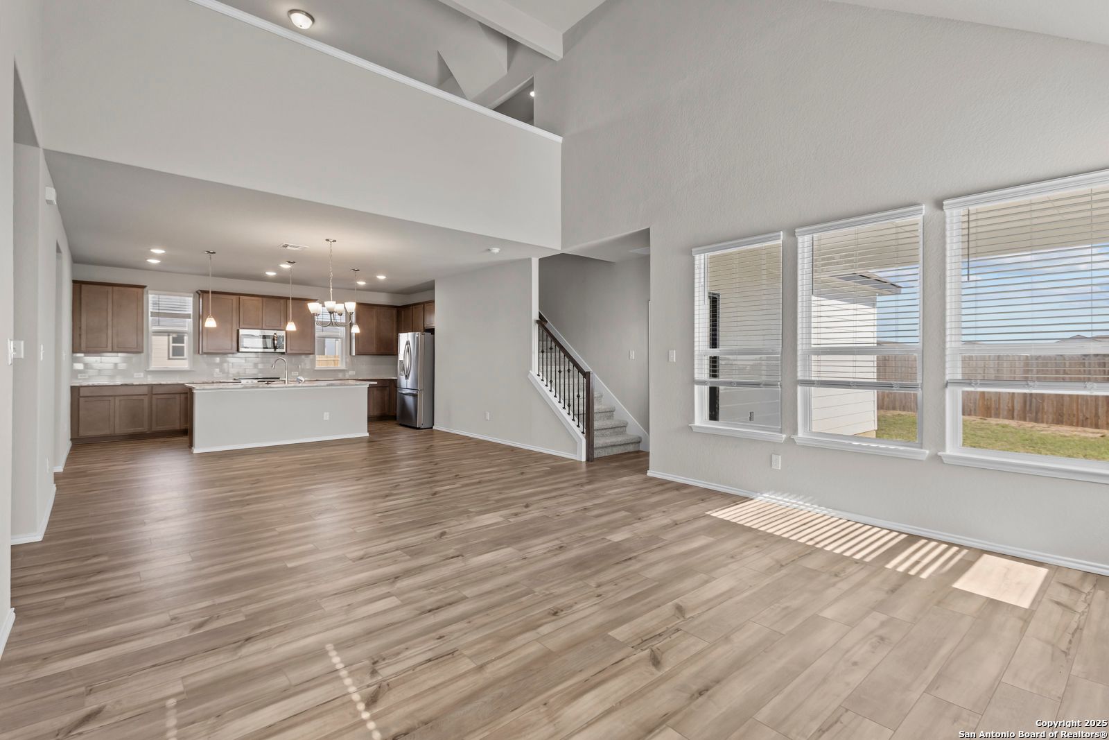 Open-concept kitchen and living area with wood floors, stainless appliances, and large windows in 3-bedroom Davidson Homes Collin B, Seguin, TX