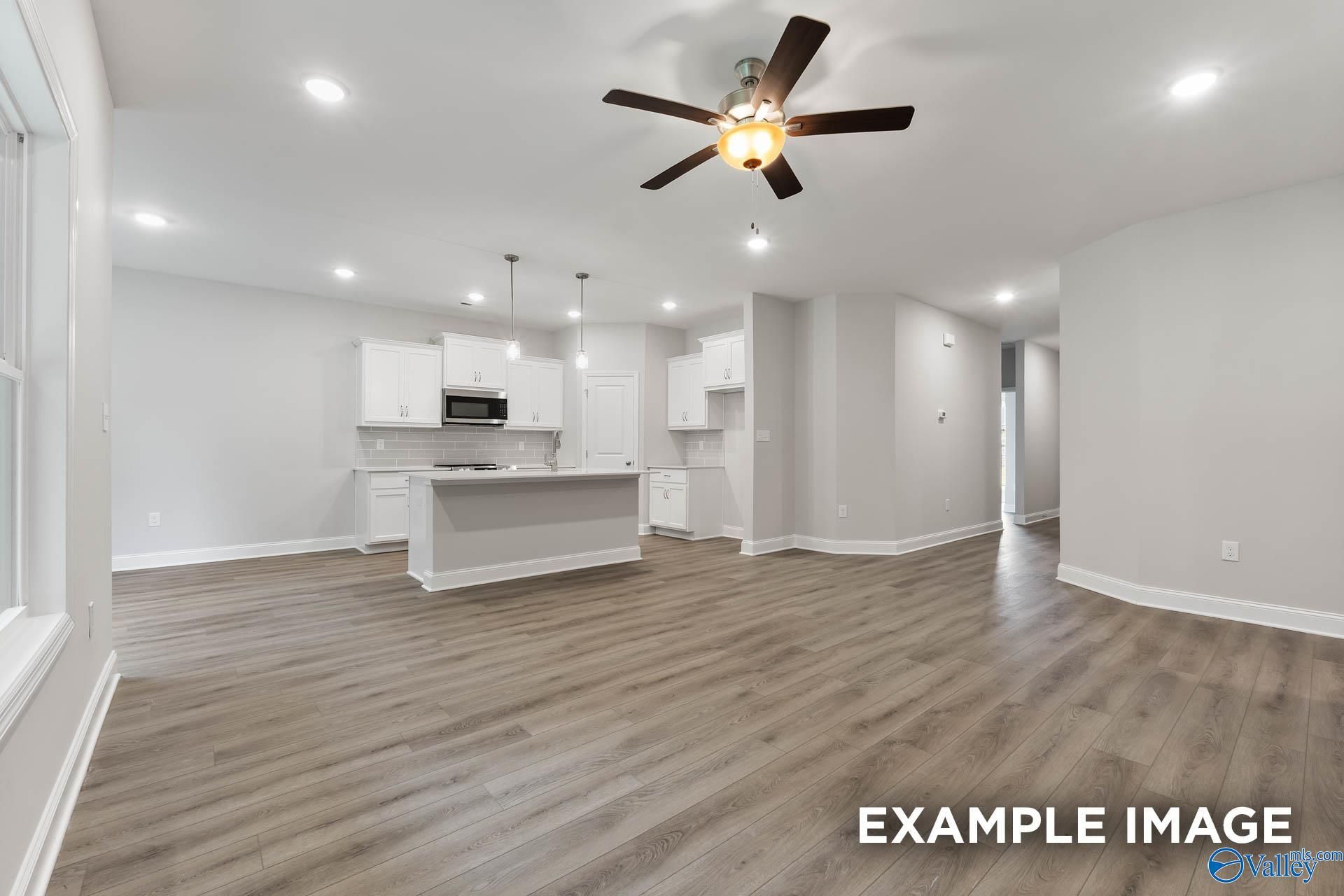 Modern open-concept kitchen with white cabinets, large island, ceiling fan, and hardwood floors in Davidson Homes Asheville C, Huntsville AL