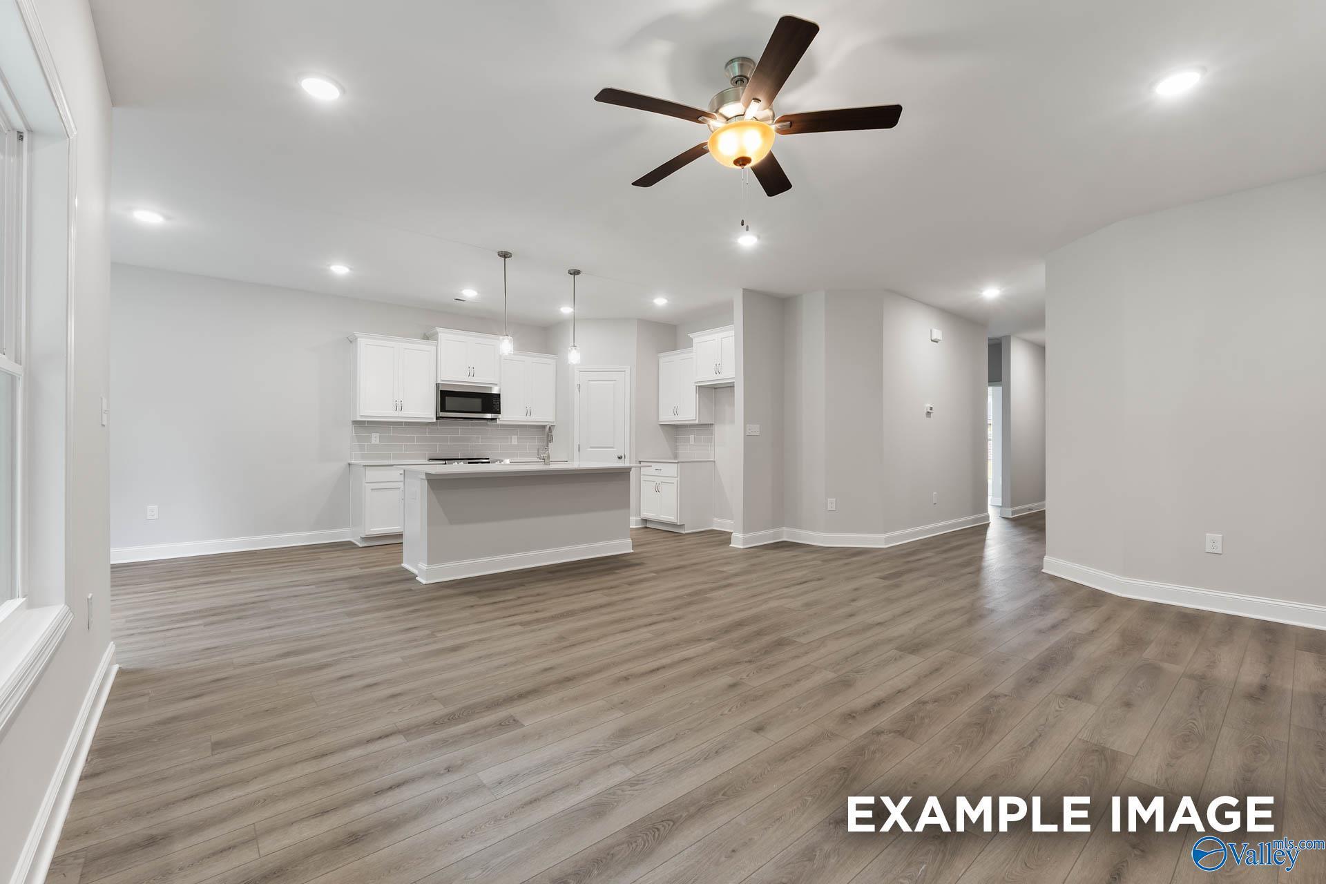 Modern open-concept kitchen with white cabinets, island, ceiling fan, and luxury vinyl plank floors in The Asheville by Davidson Homes, Huntsville AL