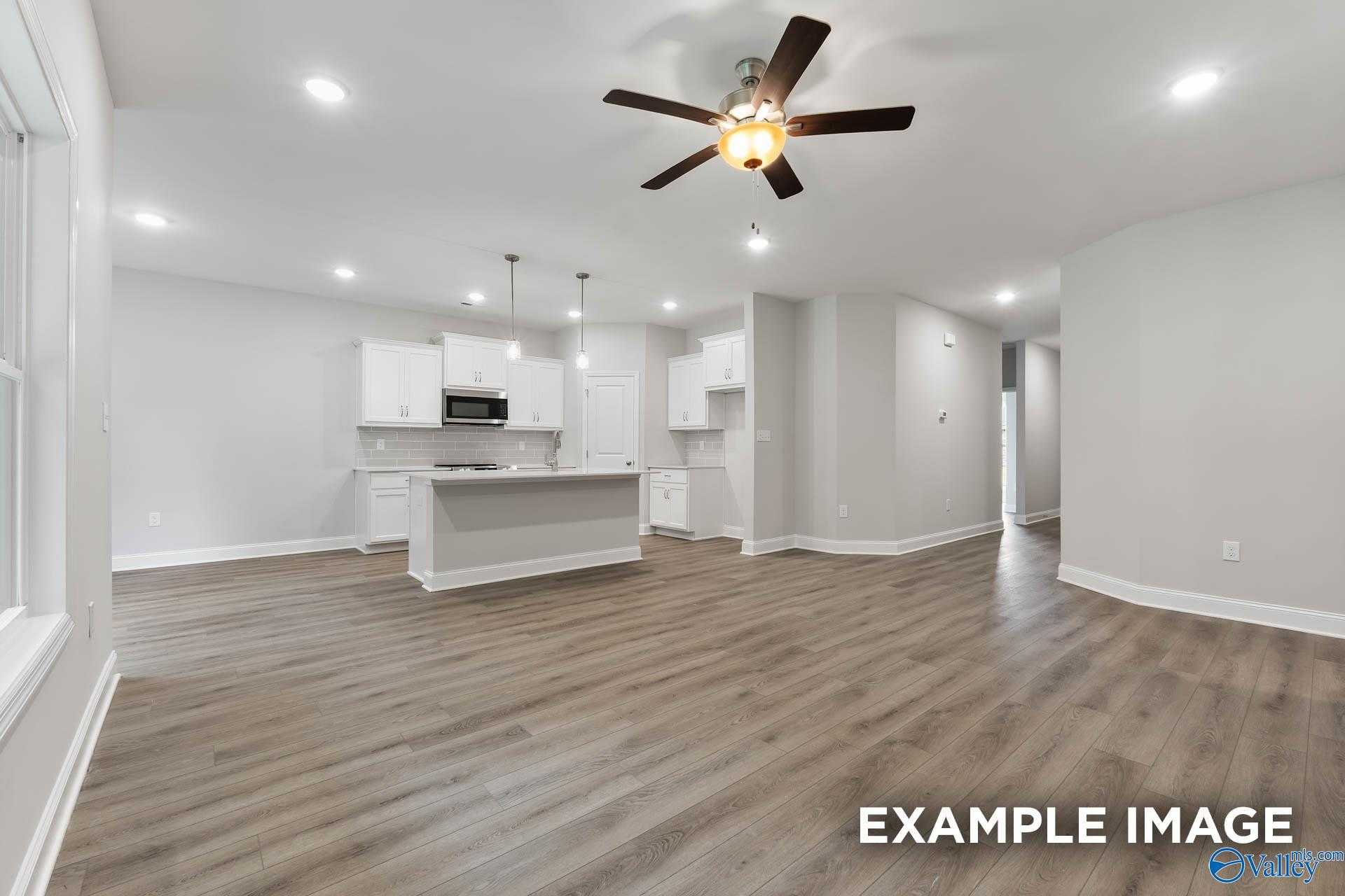 Modern open kitchen with white cabinets, large island, stainless appliances, ceiling fan, and luxury vinyl plank floors in The Asheville C, Huntsville AL