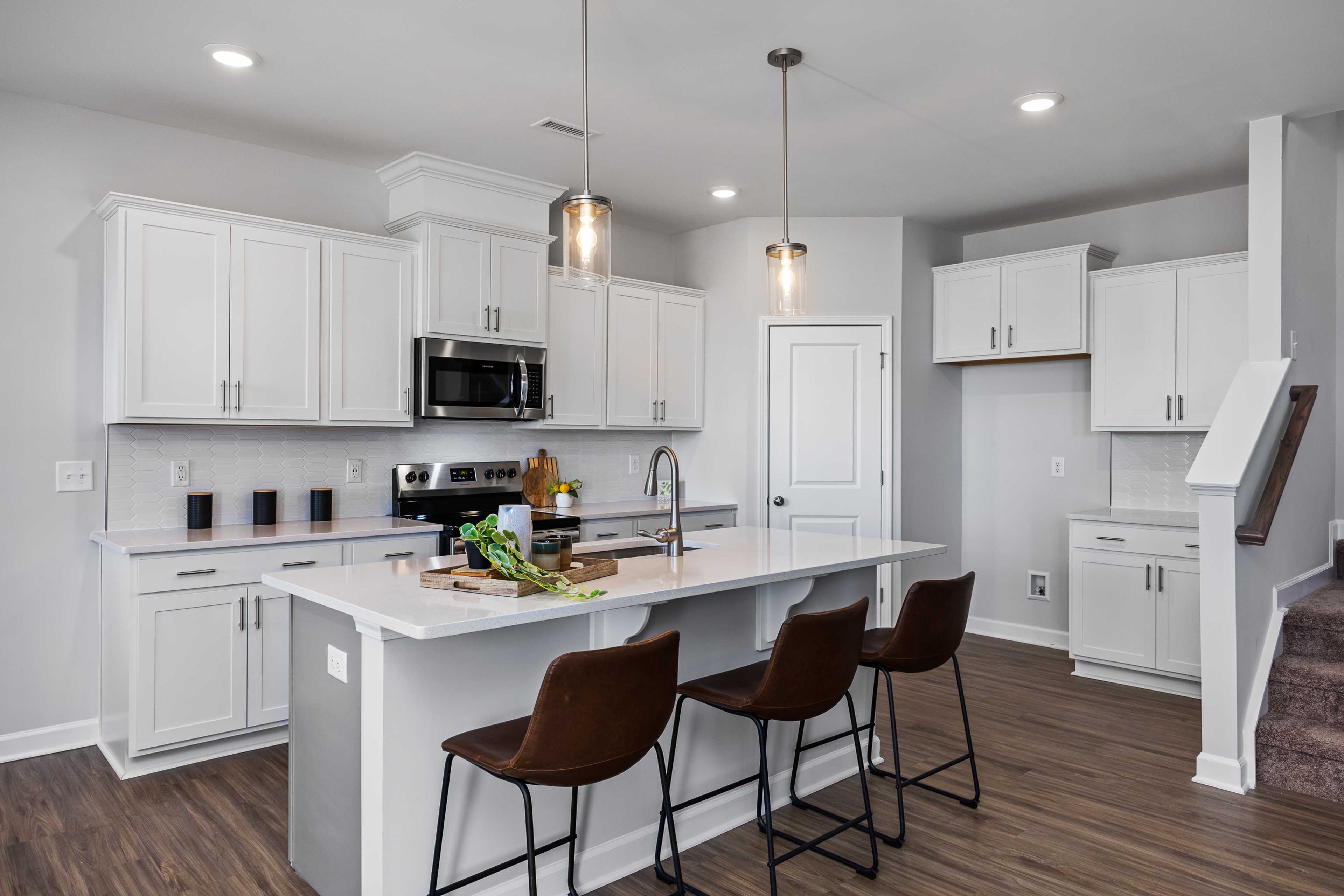 Modern kitchen in Woodland Crossing, Zebulon NC with white cabinets, quartz island, bar stools, pendant lights, and hardwood floors