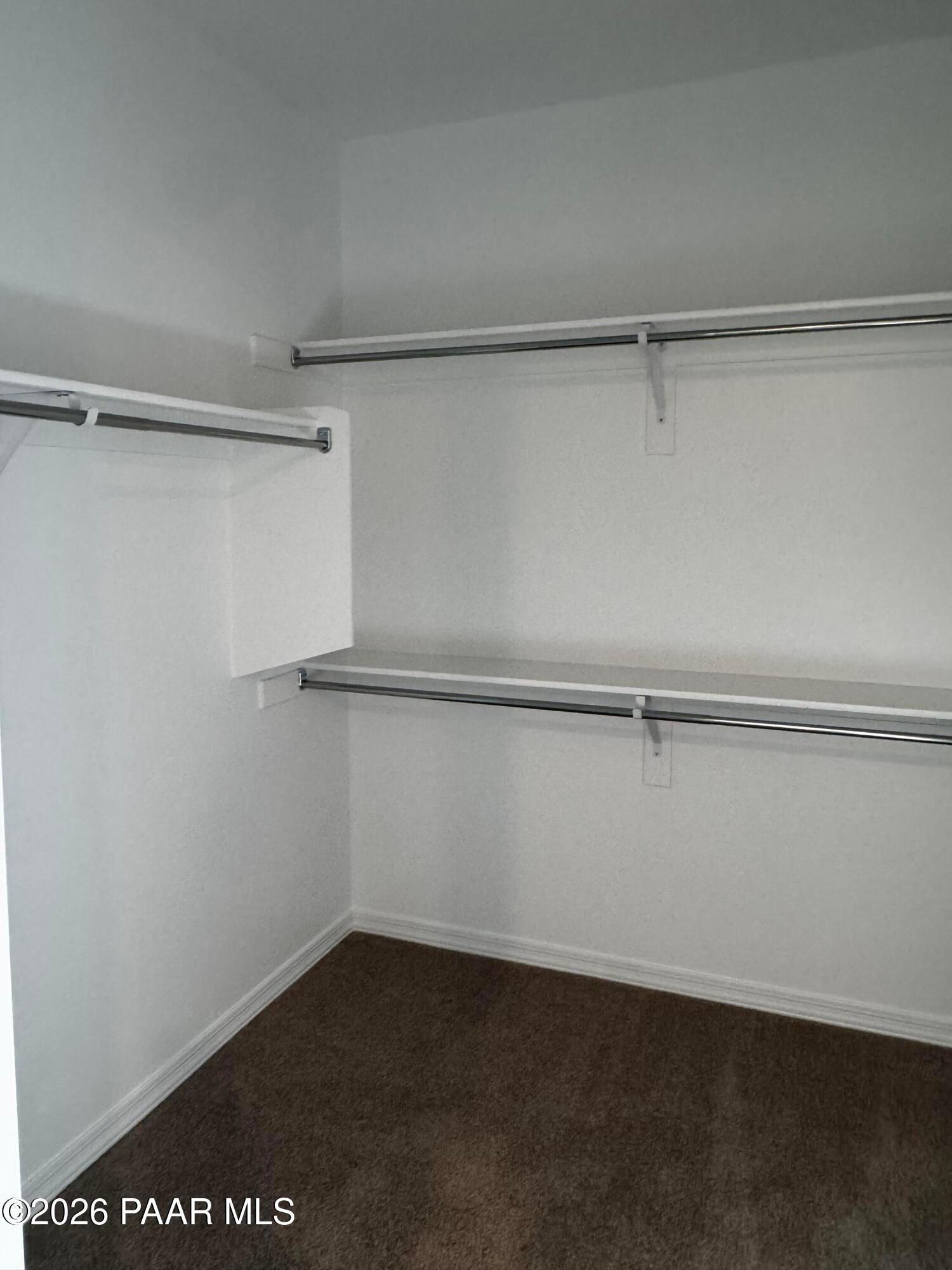 Spacious walk-in closet with white walls, wooden shelves, and hanging rods on brown carpet in Davidson Homes Durango II B, Prescott AZ