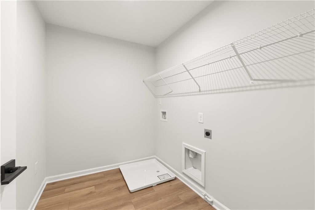 White laundry room with wire shelving, utility hookups, and hardwood floors in 3-bedroom Cary A home, Winder, Georgia