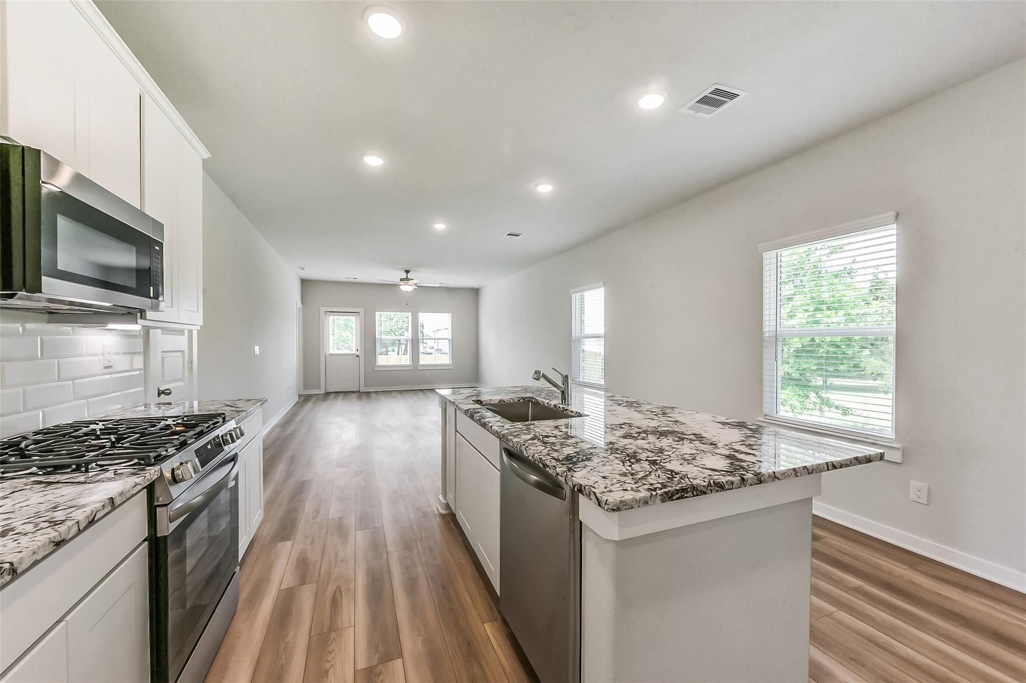 Modern open-concept kitchen featuring granite countertops, stainless steel appliances, and island sink in Davidson Homes The Frio G, Magnolia Texas