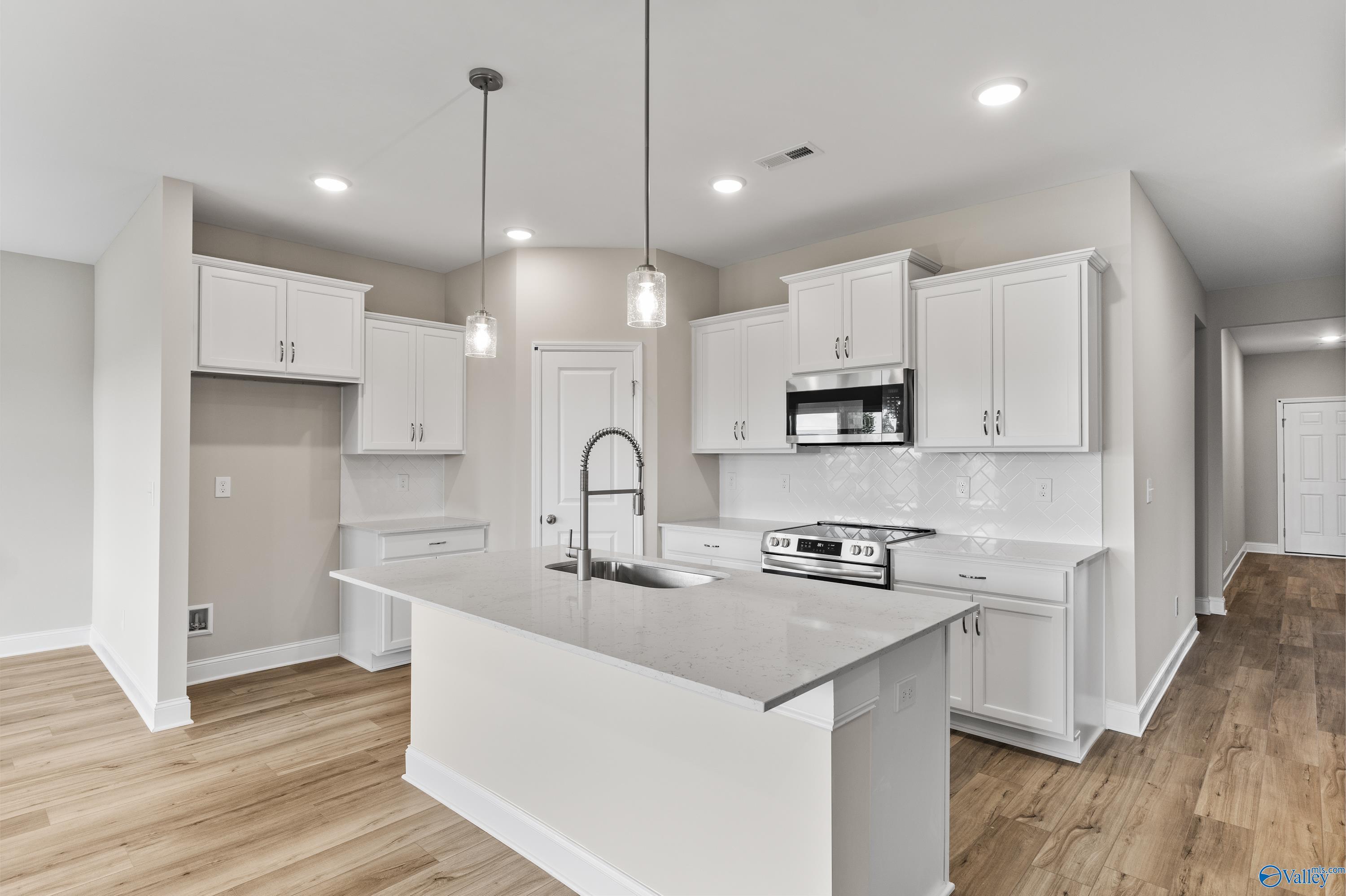 Modern white kitchen island with quartz counters, stainless appliances, and pendant lights in The Daphne C floor plan, Harvest, AL