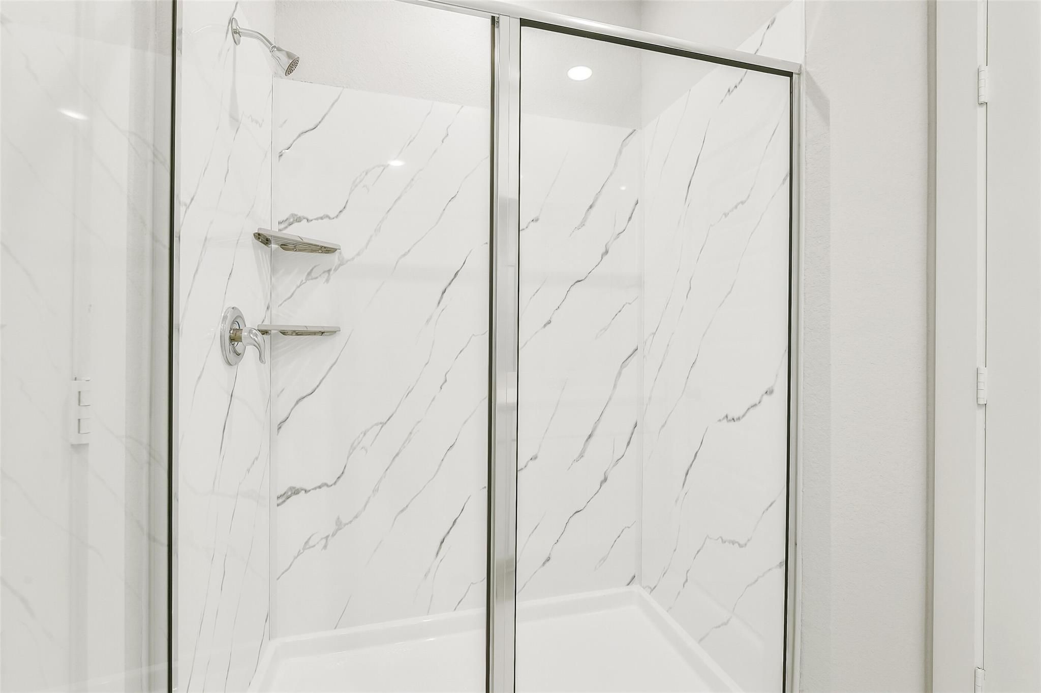 Elegant frameless glass walk-in shower with white marble-look tile walls in master bath of Davidson Homes The San Marcos E, Cleveland, Texas