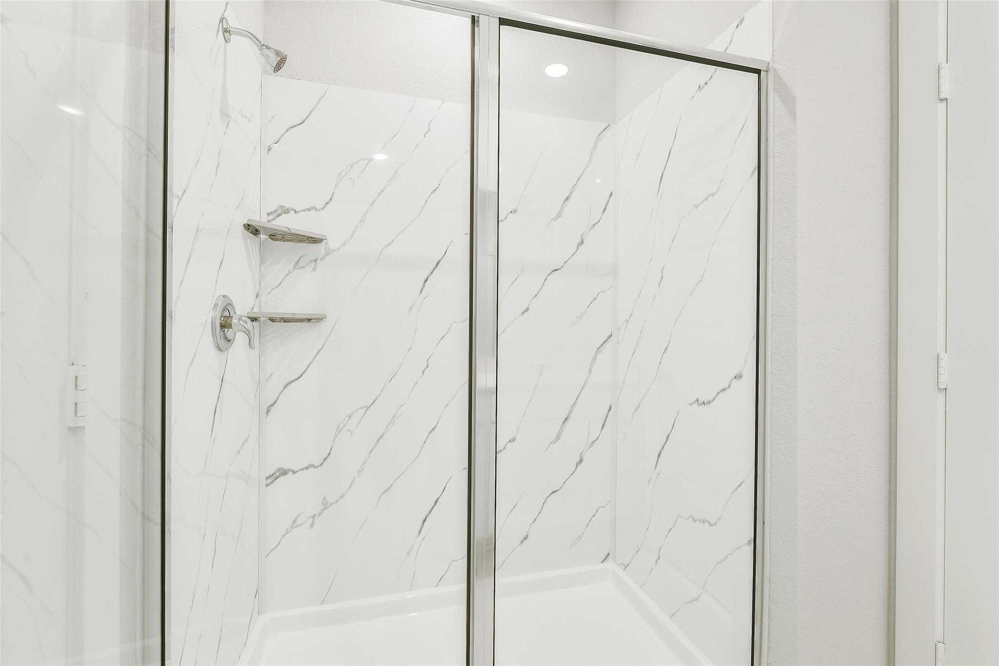 Elegant frameless glass walk-in shower with white marble-look tile walls in master bath of Davidson Homes The San Marcos E, Cleveland, Texas