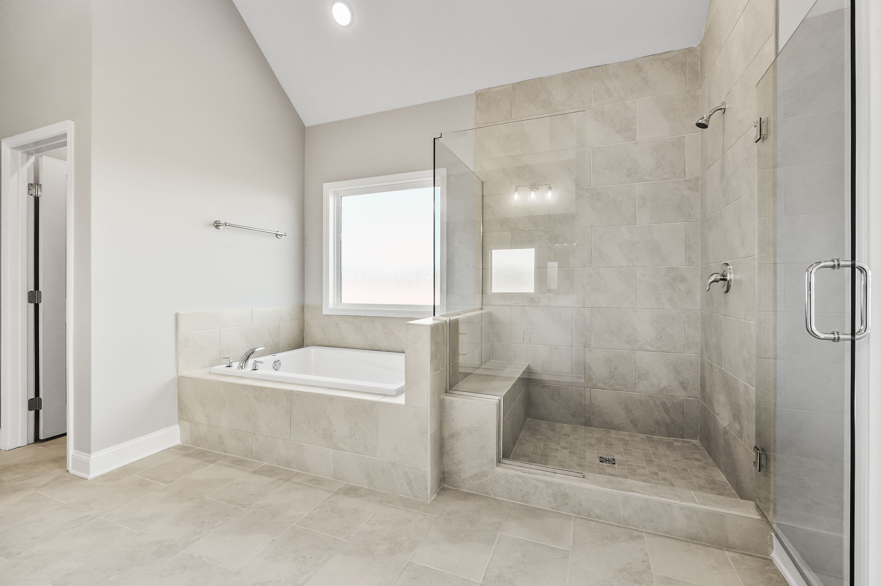 Spacious master bathroom in The Valencia with freestanding tub, glass shower enclosure, tiled walls, and natural light window