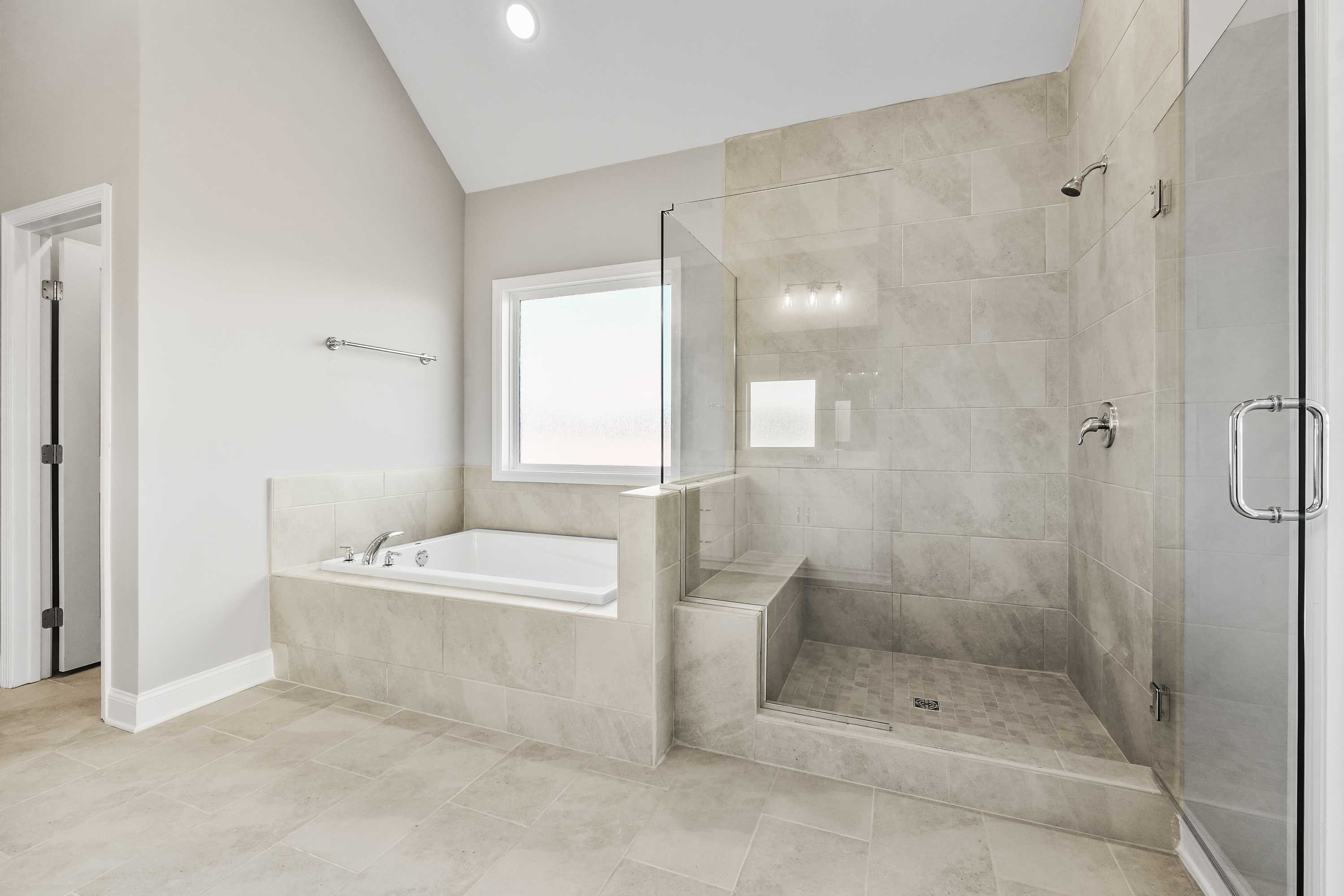 Spacious master bathroom in The Valencia with freestanding tub, glass shower enclosure, tiled walls, and natural light window