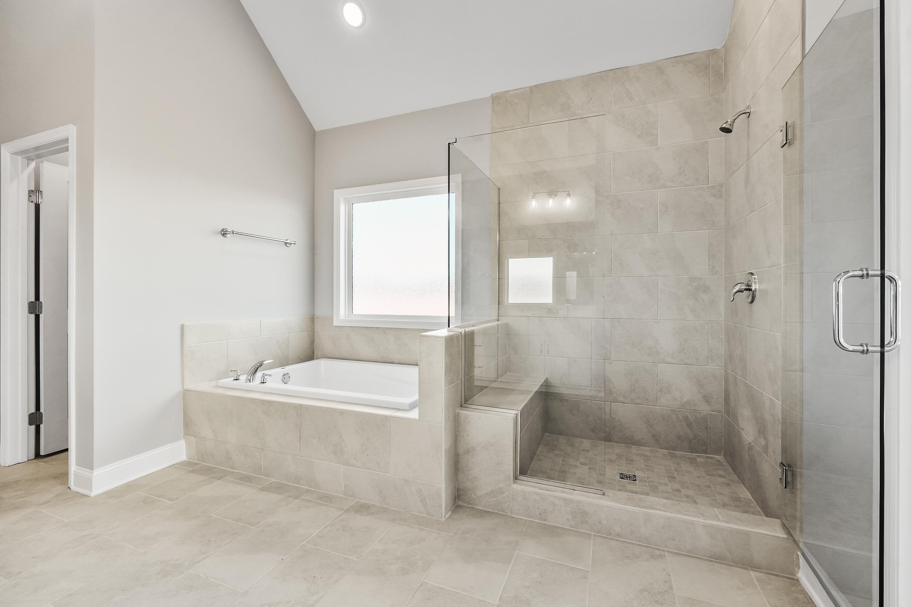 Spacious master bathroom in The Valencia with freestanding tub, glass shower enclosure, tiled walls, and natural light window