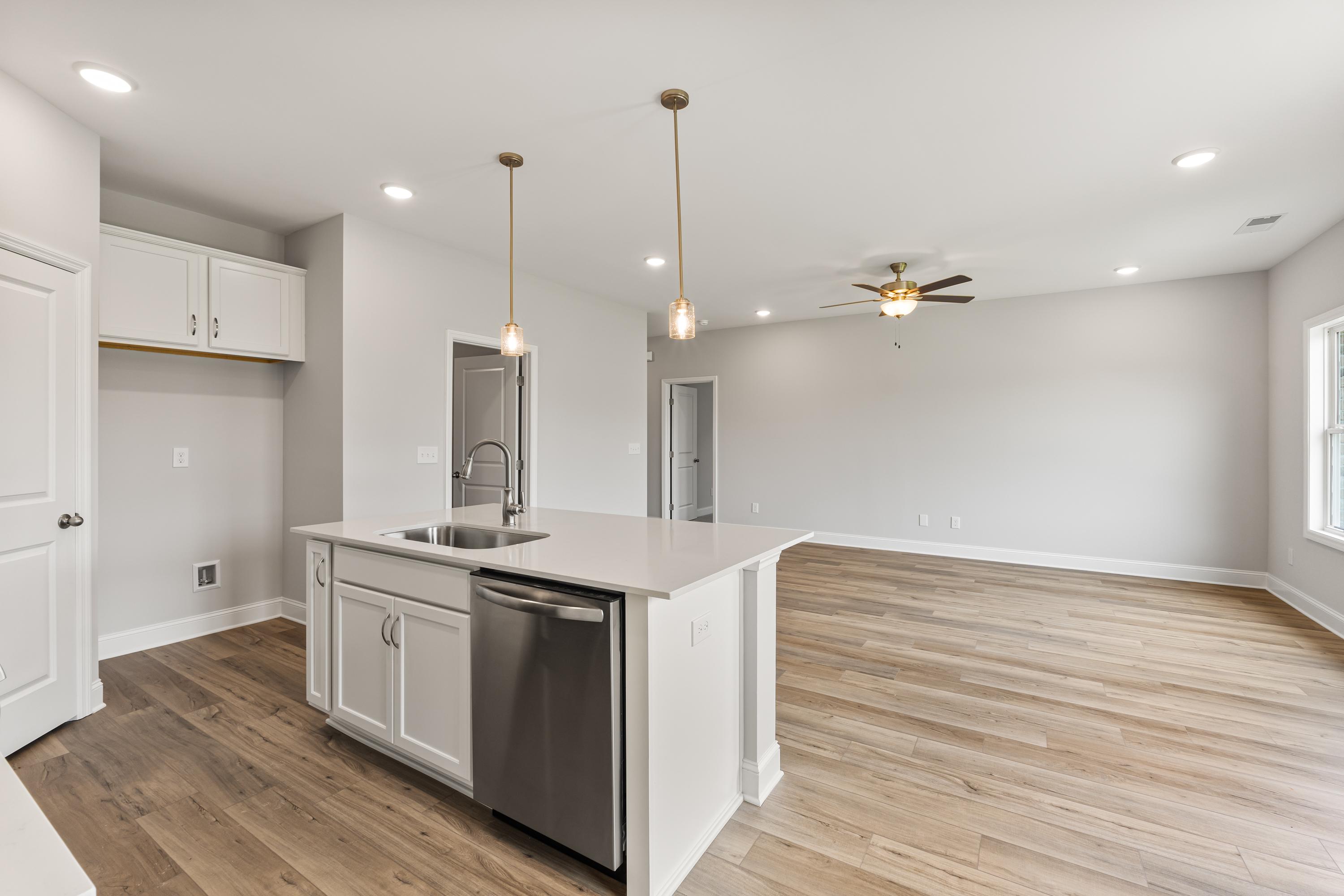 Modern kitchen in The Butler home design with white island, stainless dishwasher, pendant lights, and open hardwood living area