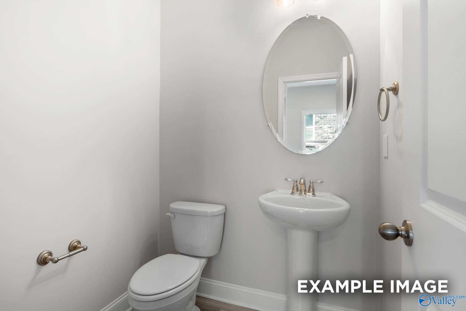 Cozy powder room with round mirror over pedestal sink and white toilet in The Camden floor plan, Huntsville, Alabama