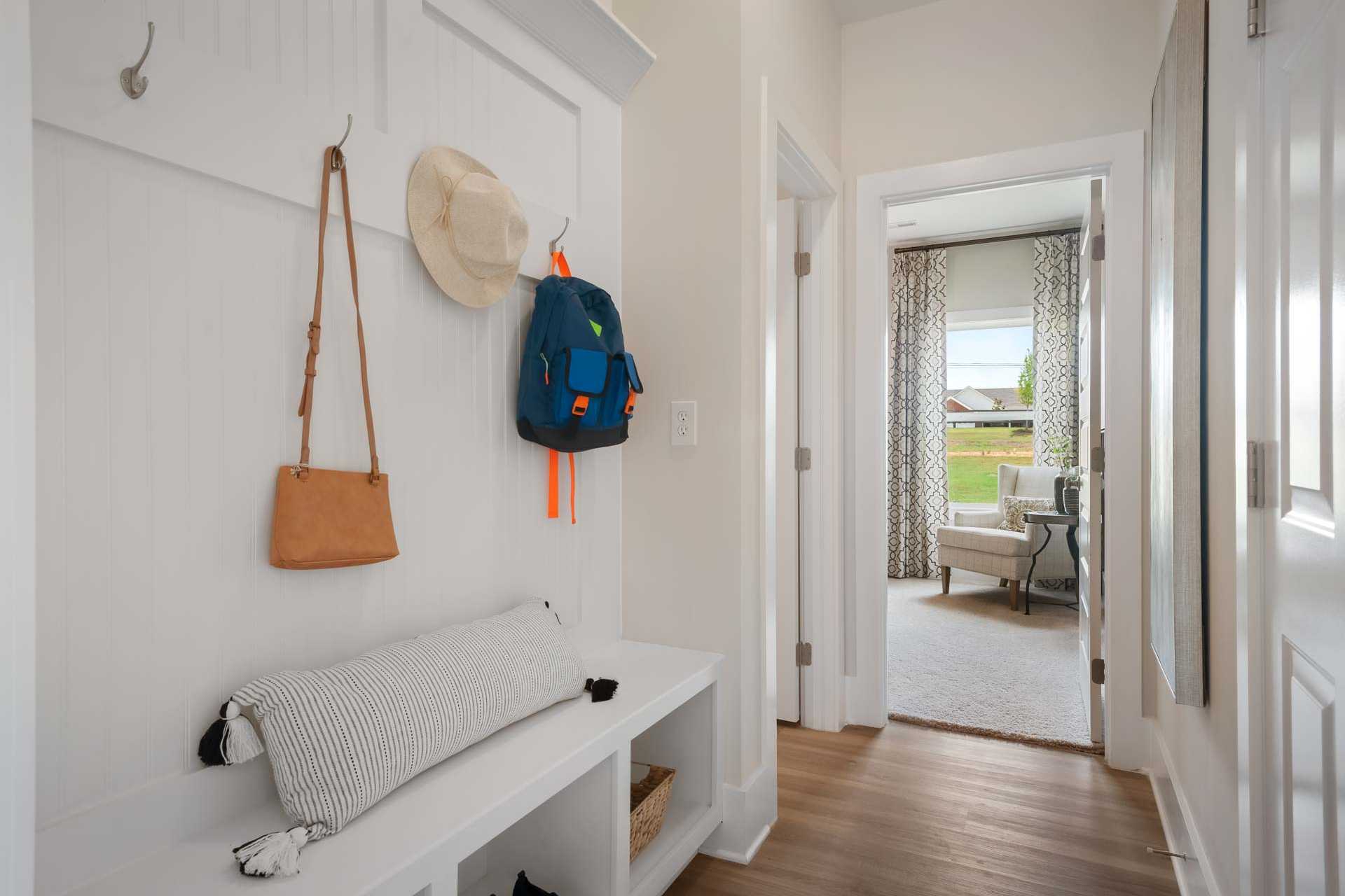 White shiplap mudroom entry at Flint Meadows in New Market, Alabama with hooks, backpack, hat, cushioned bench, and hardwood floors