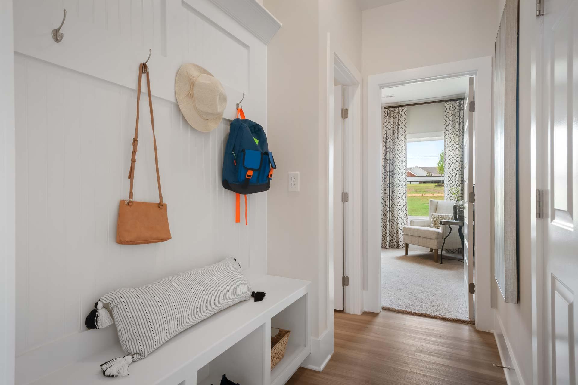 White shiplap mudroom entry at Flint Meadows in New Market, Alabama with hooks, backpack, hat, cushioned bench, and hardwood floors