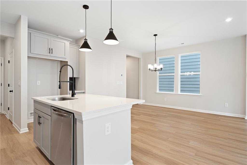 Modern open-concept kitchen with white quartz island, black faucet, stainless dishwasher, and hardwood floors in Davidson Homes The Marion A, Kennesaw, GA