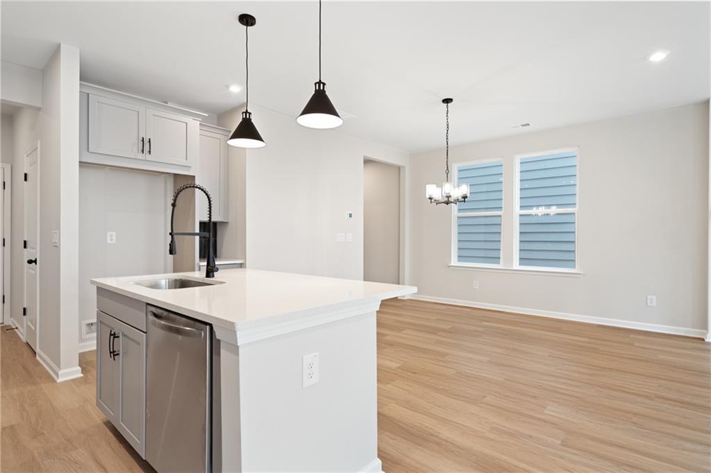 Open-concept kitchen with white quartz island, sink, stainless dishwasher, and pendant lights in The Marion A, Kennesaw, Georgia