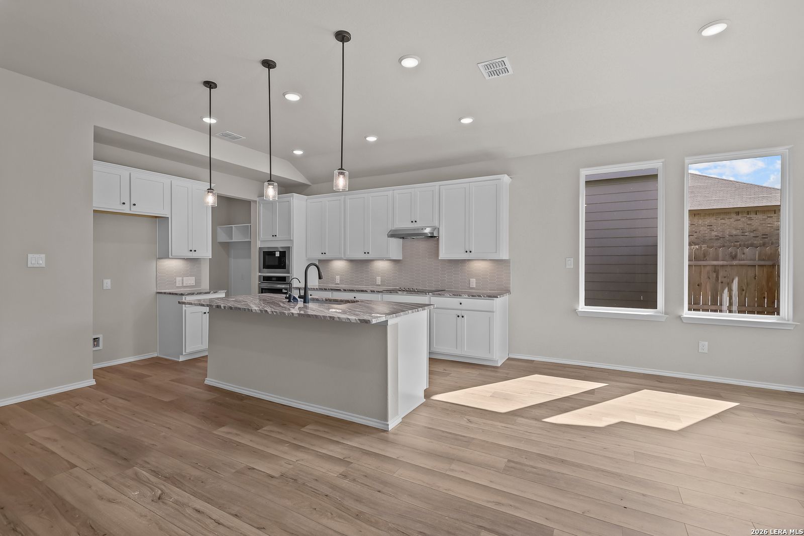 Open-concept kitchen with white shaker cabinets, granite island, pendant lights, and hardwood floors in Davidson Homes Sequoia C, San Antonio