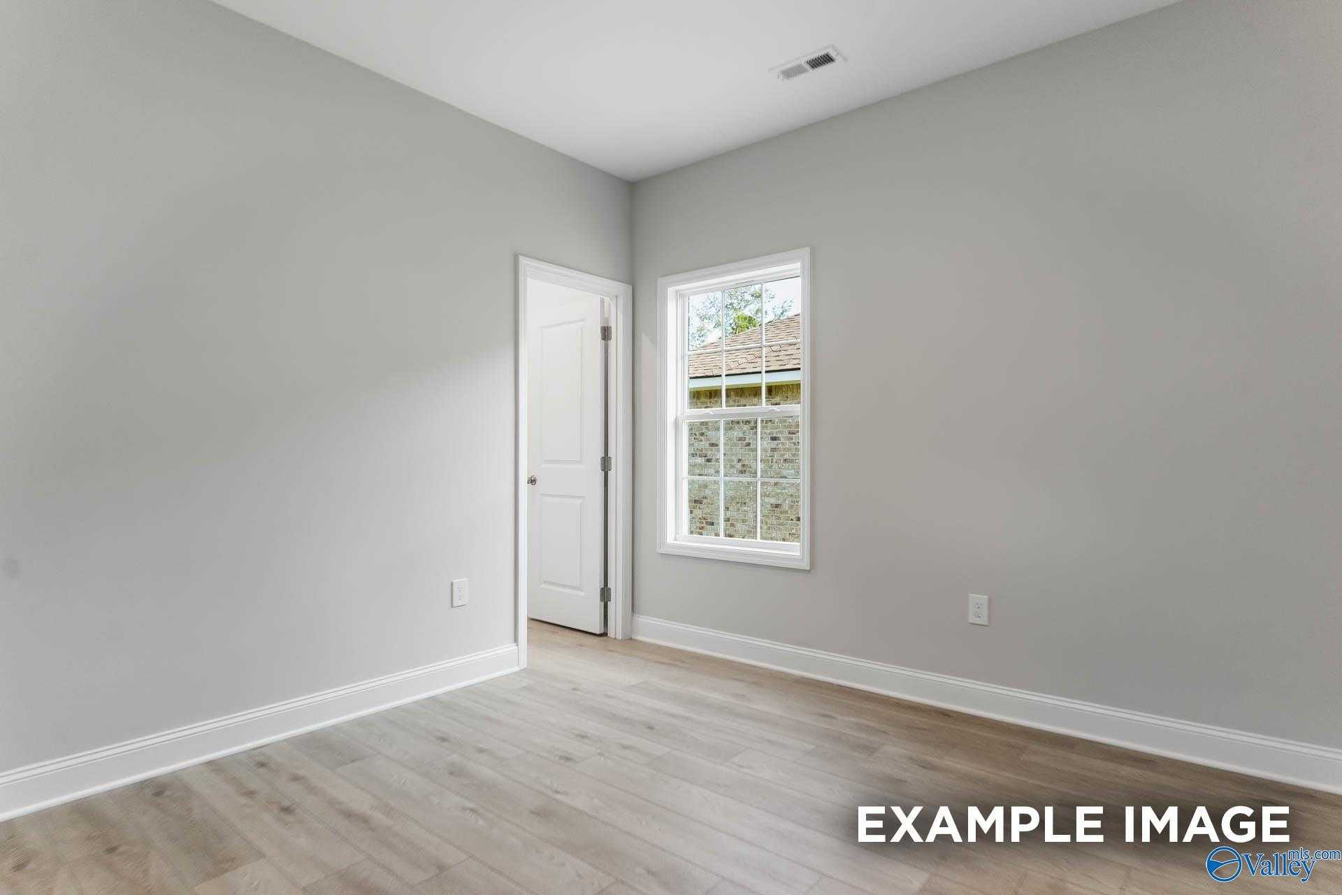 Bright empty bedroom with gray walls, light wood floors, white door, and window view in Davidson Homes The Daphne C, New Market, Alabama