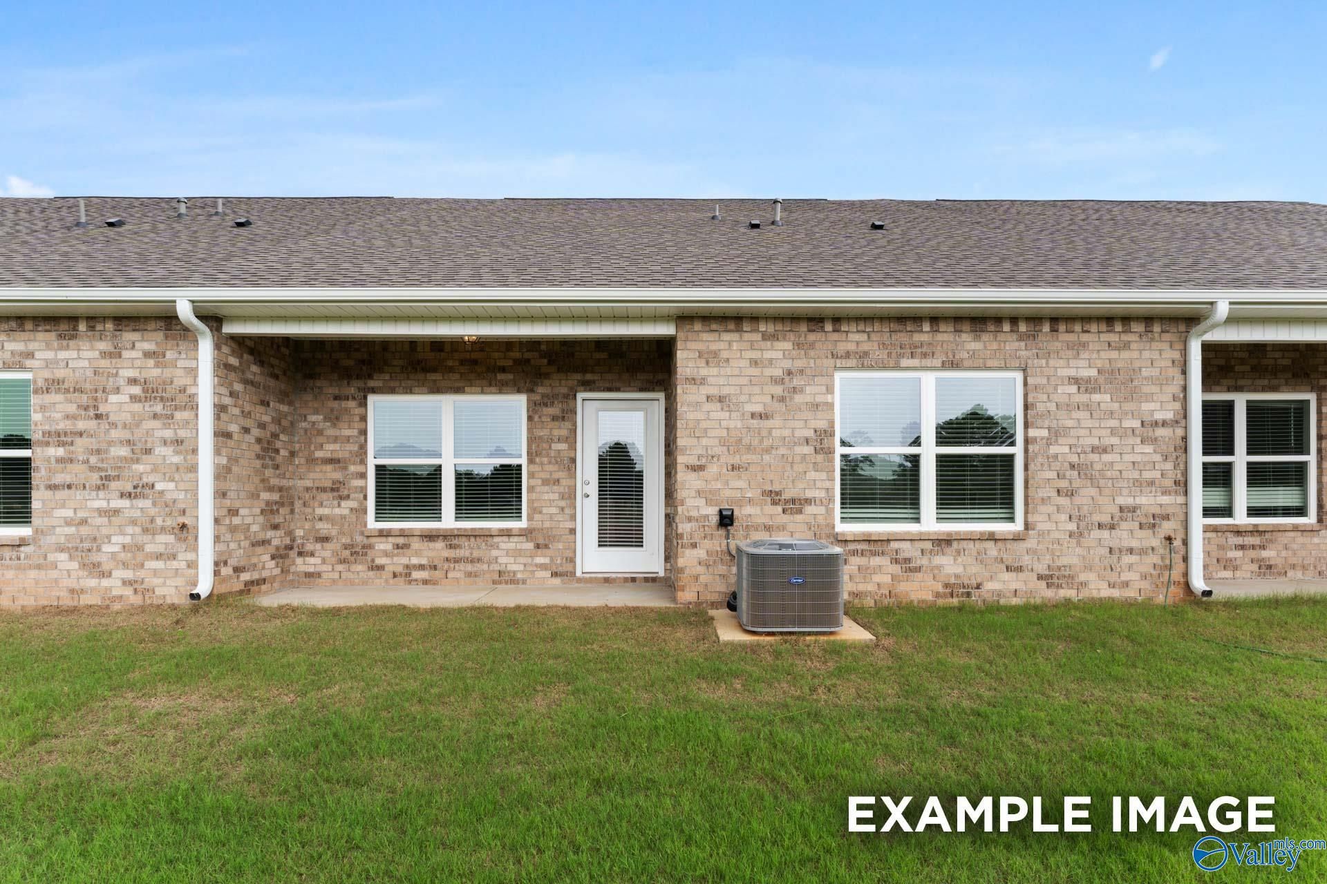 Covered back patio on brick single-story home with large windows, AC unit, and green yard in Davidson Homes The Cumberland B, Decatur, Alabama