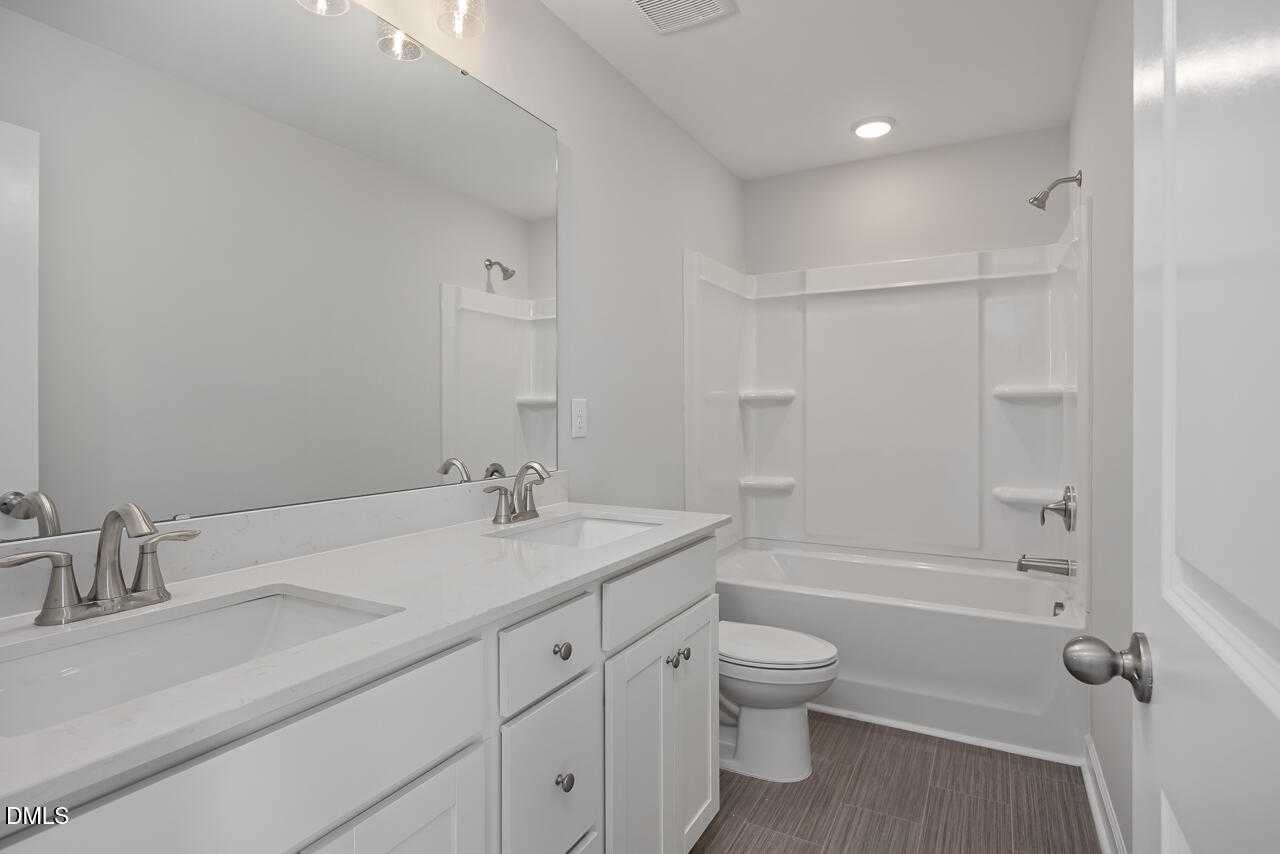 Modern bathroom with white double vanity, soaking tub, shower, and toilet in Davidson Homes The Graham, Fuquay-Varina, NC