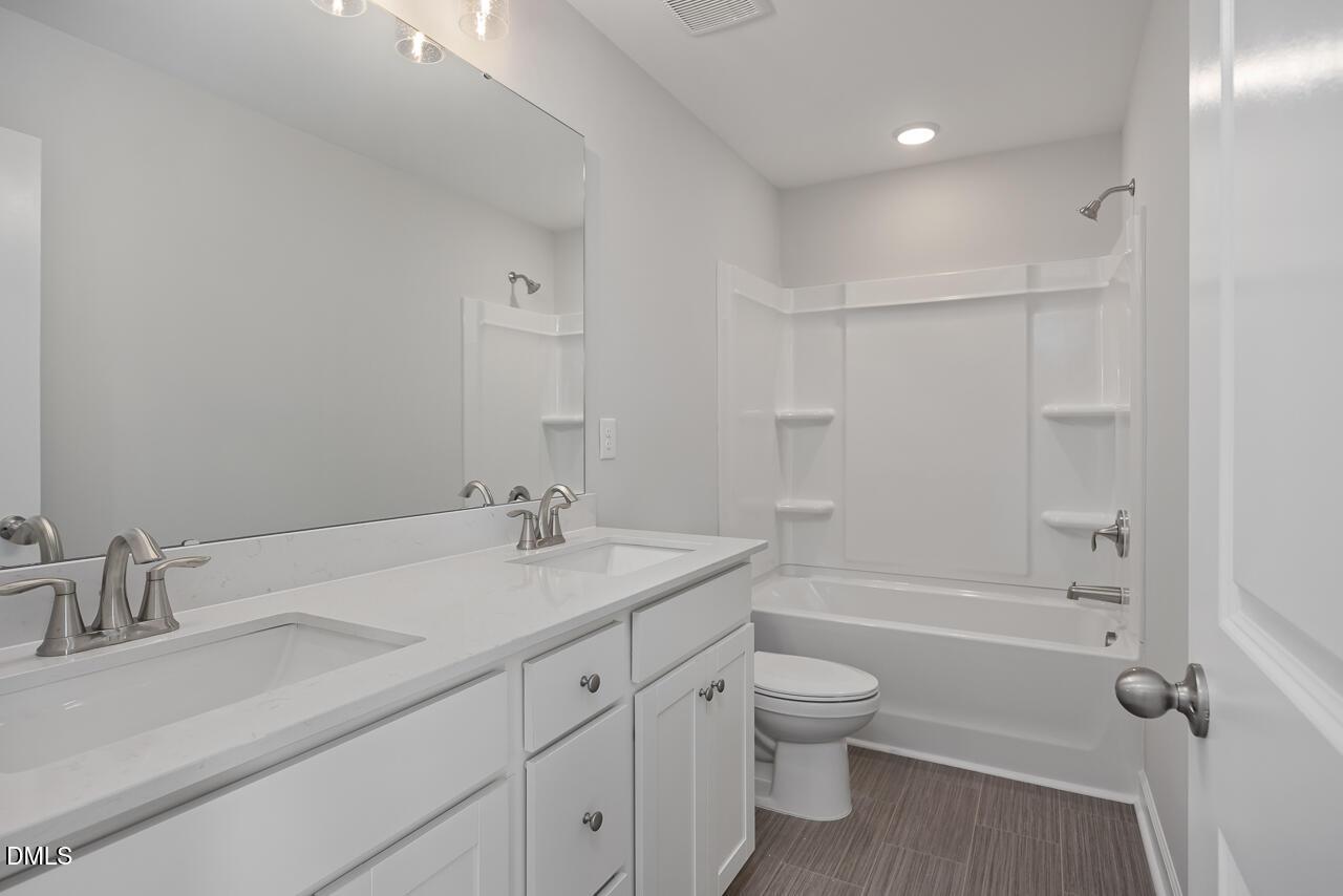 Modern full bathroom with double vanity, white cabinets, and shower-tub combo in The Graham floor plan, Springvale, NC.