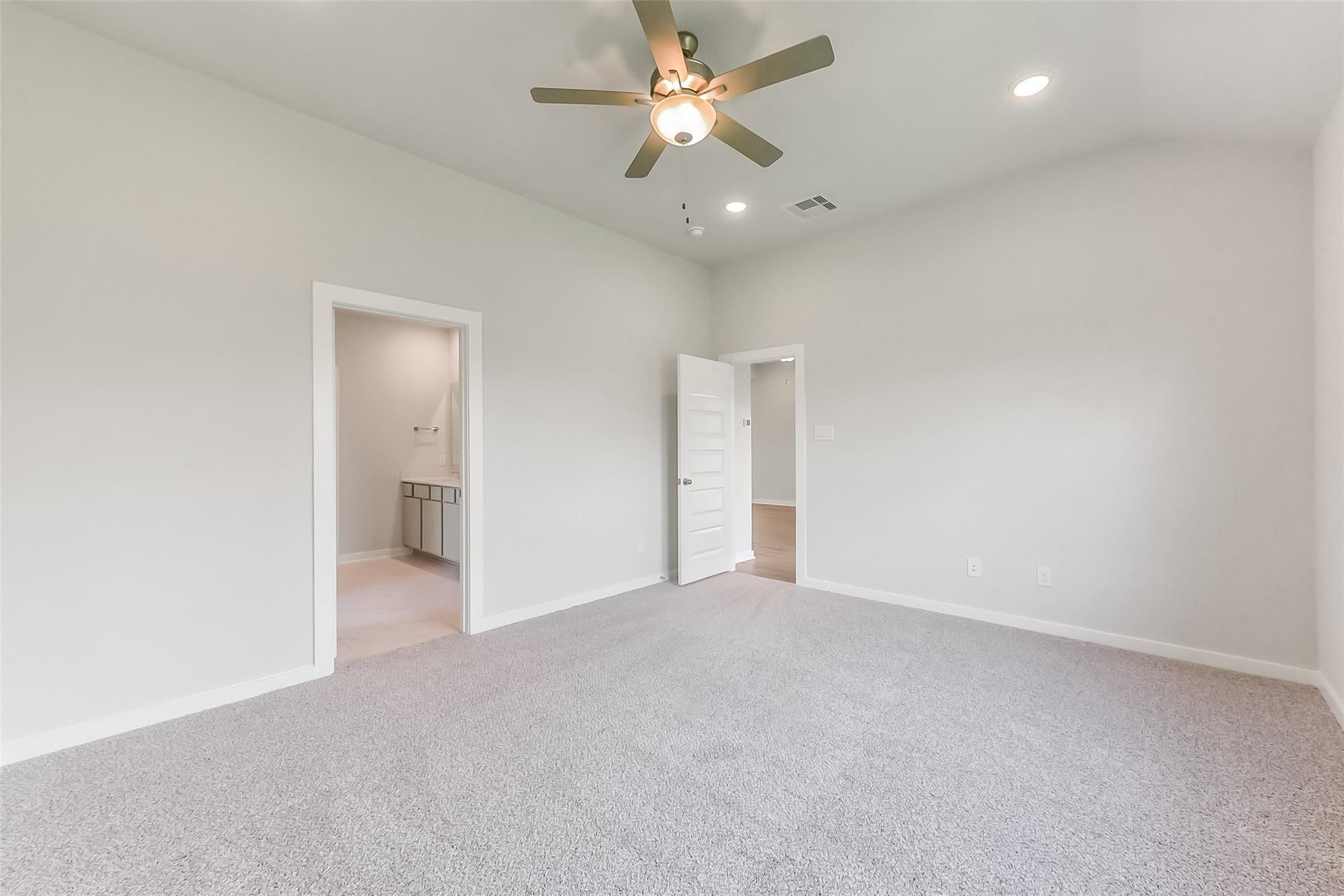 Spacious master bedroom with ceiling fan, en-suite bath vanity, and carpet flooring in Davidson Homes The Tierra C, Dayton, Texas