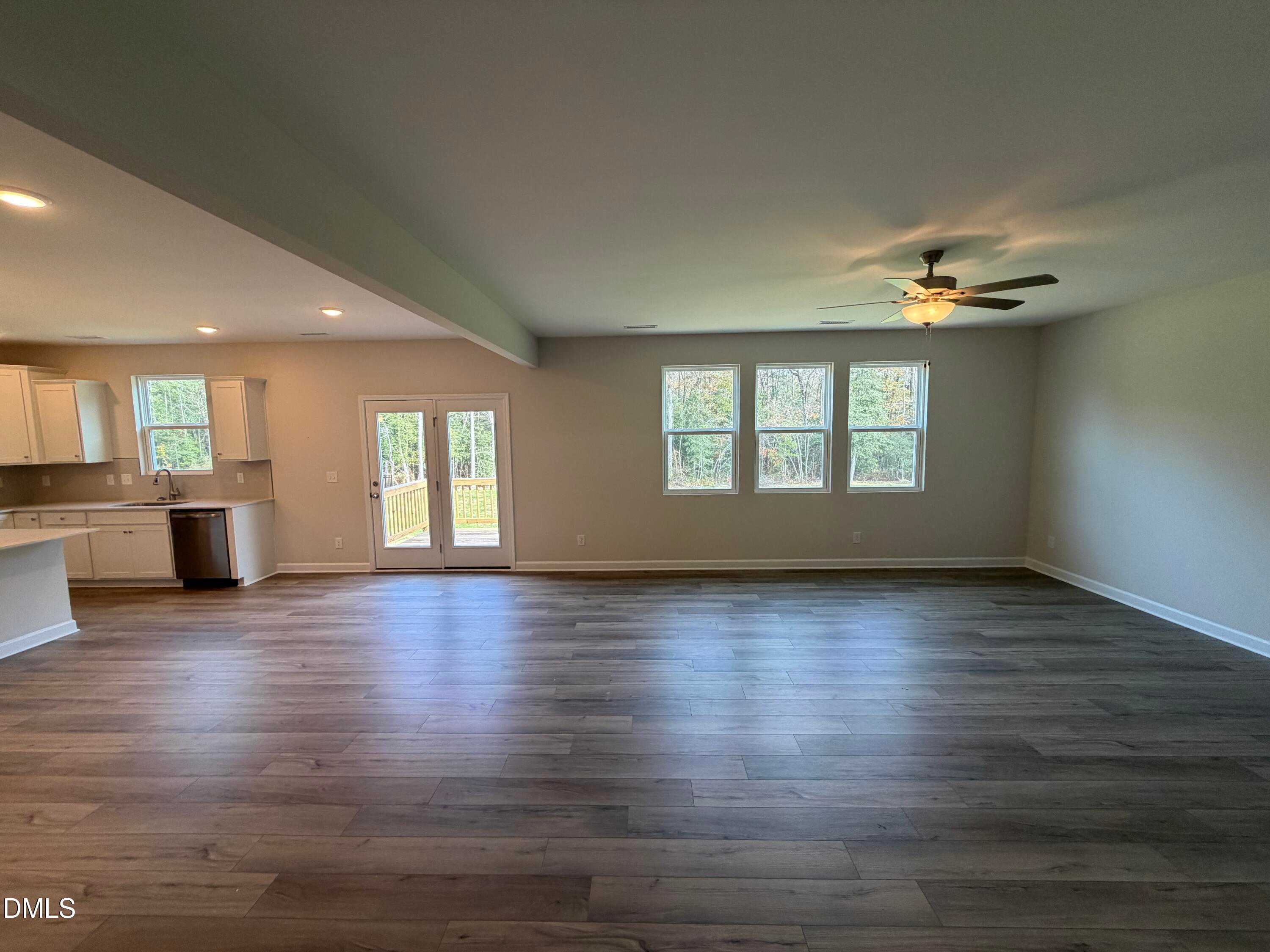 Spacious open-concept living room with laminate flooring, ceiling fan, large windows, and French doors to patio in Davidson Homes The Hickory II A, Lillington, NC