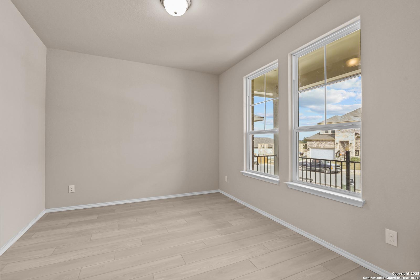 Bright empty room with beige walls, light wood floors, and large windows overlooking porch in Davidson Homes The Douglas G, San Antonio