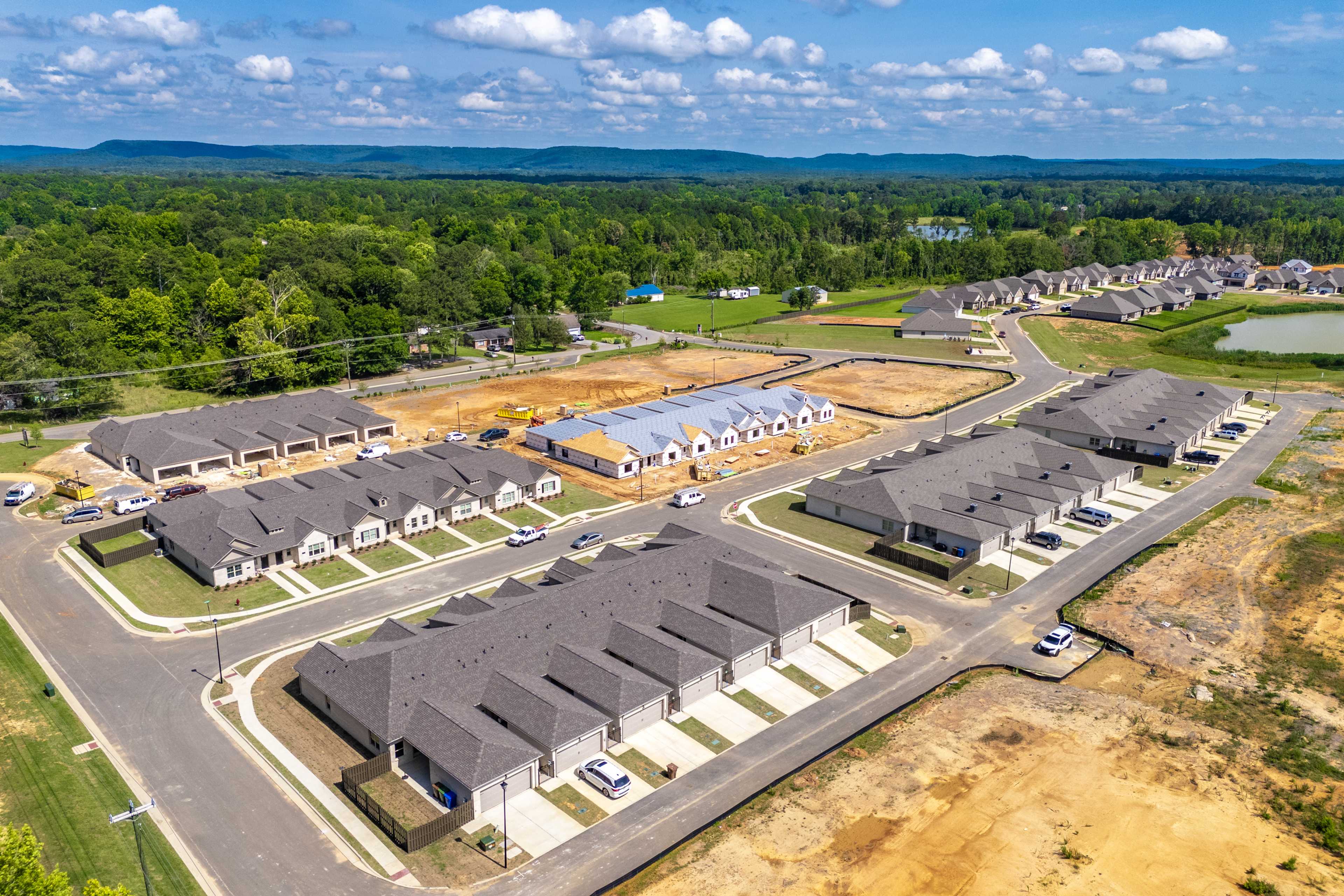 Aerial view of new townhomes under construction at The Retreat at Cain Park in Hartselle Alabama with wooded surroundings and pond