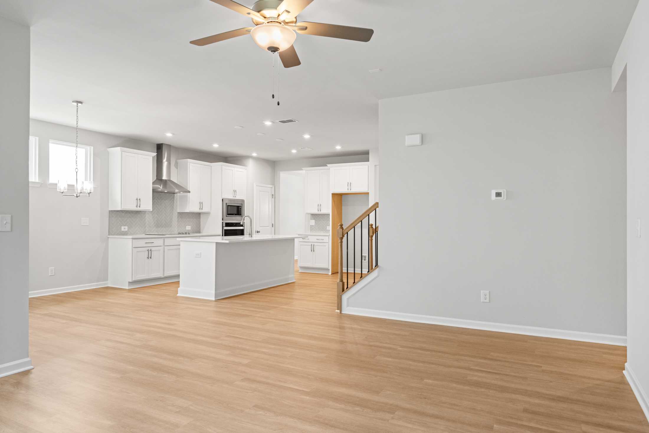 Open-concept kitchen in The Ash B showcasing white shaker cabinets, large center island, stainless appliances, and hardwood floors