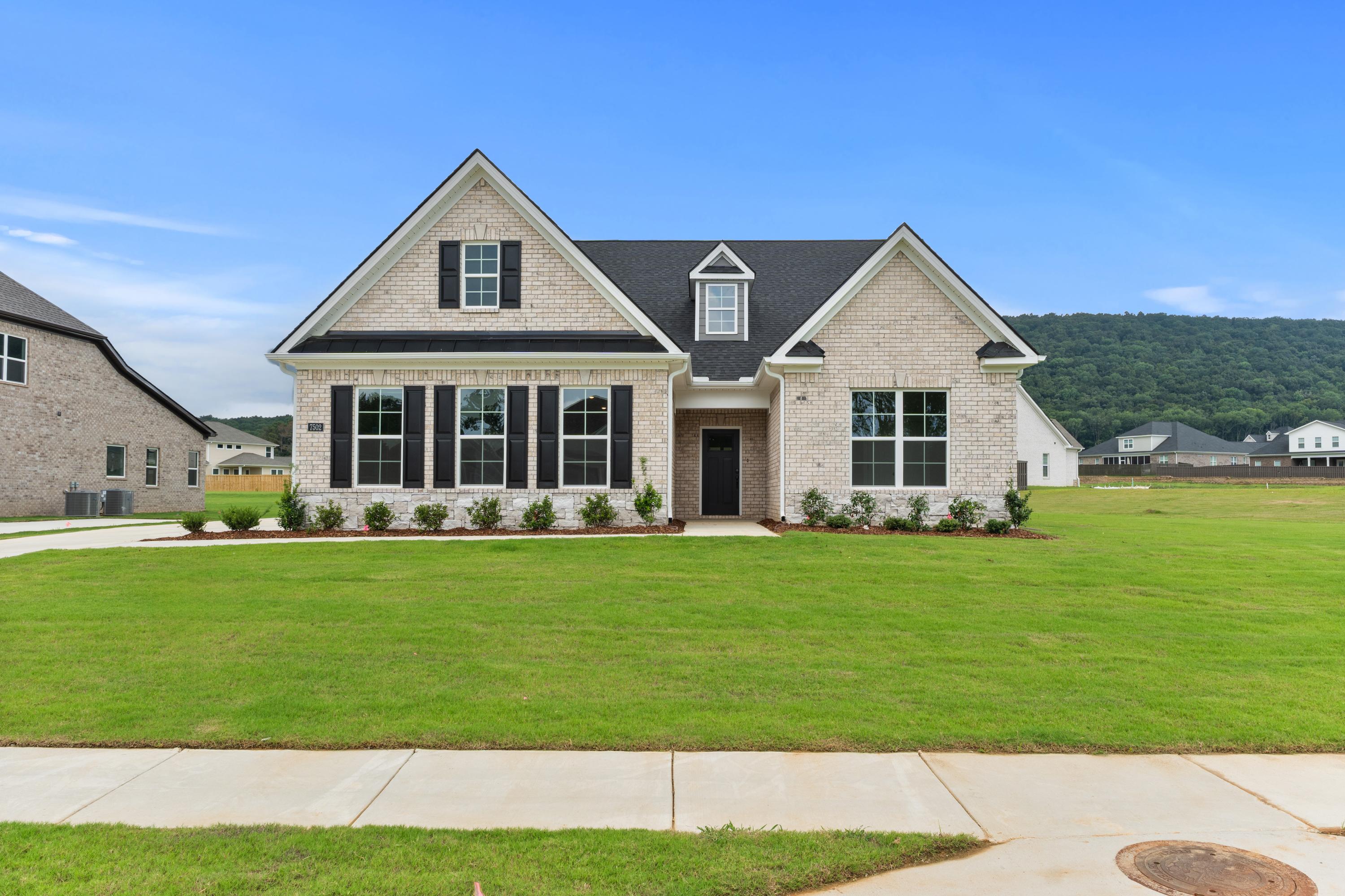 Two-story brick elevation of The Oxford showcasing gabled roof, black shutters, covered porch, lush lawn in Owens Cross Roads