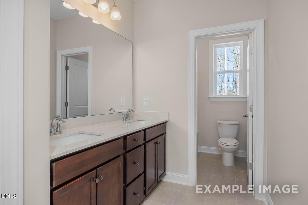 Elegant master bathroom double vanity with dark wood cabinets, large mirror, and separate toilet in Davidson Homes The Crawford D, Angier, NC